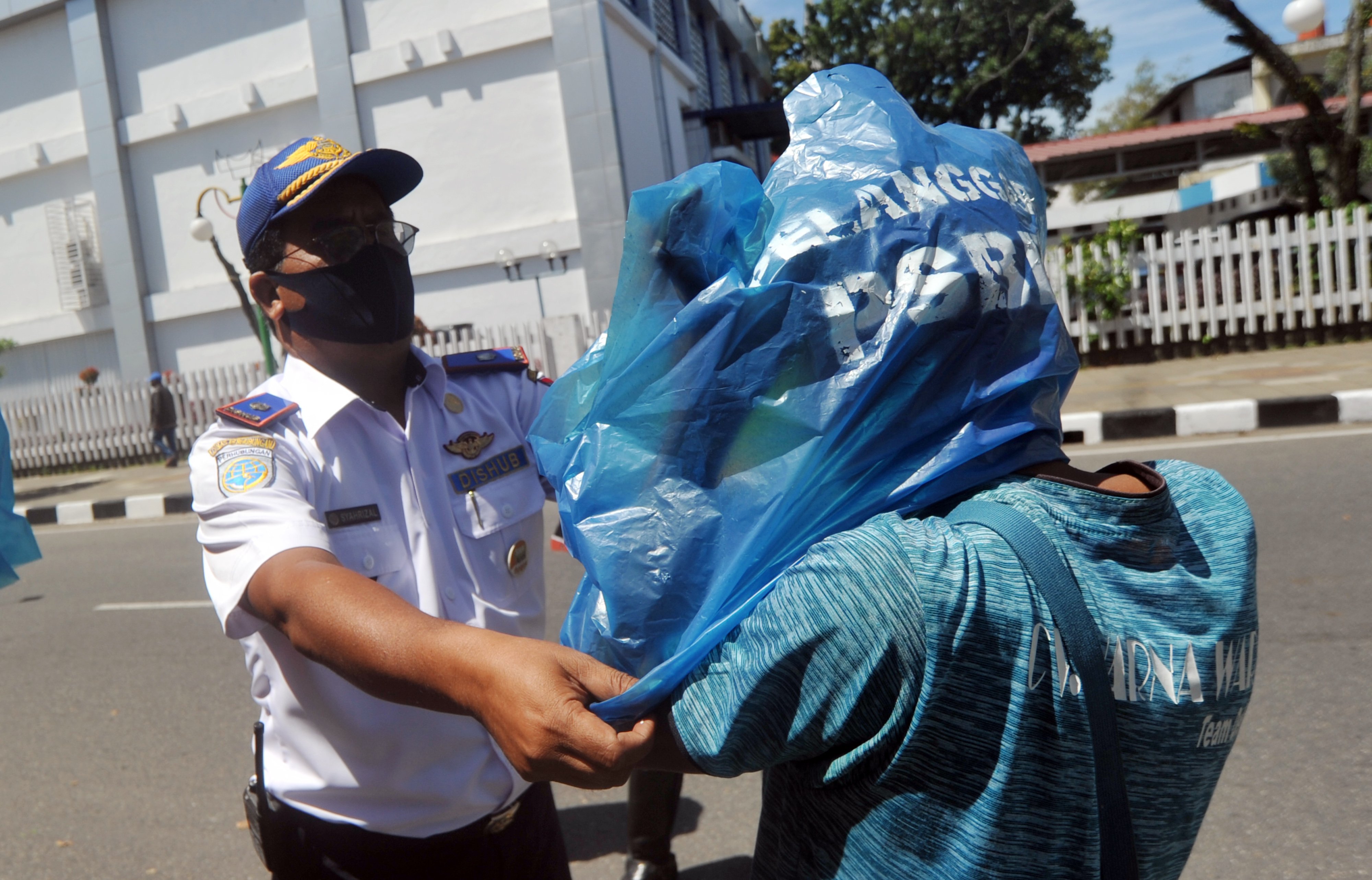 Petugas memasangkan rompi plastik kepada warga yang tidak menggunakan masker, di Pasar Raya, Padang, Sumatra Barat, Selasa (12/5).
