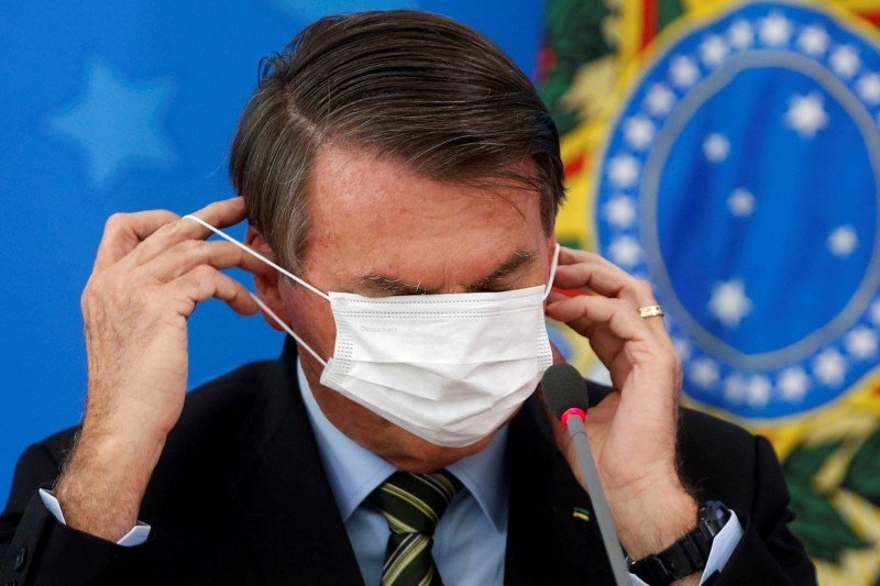 Presiden Brasil Jair Bolsonaro memperbaiki maskernya saat memberikan keterangan kepada media.