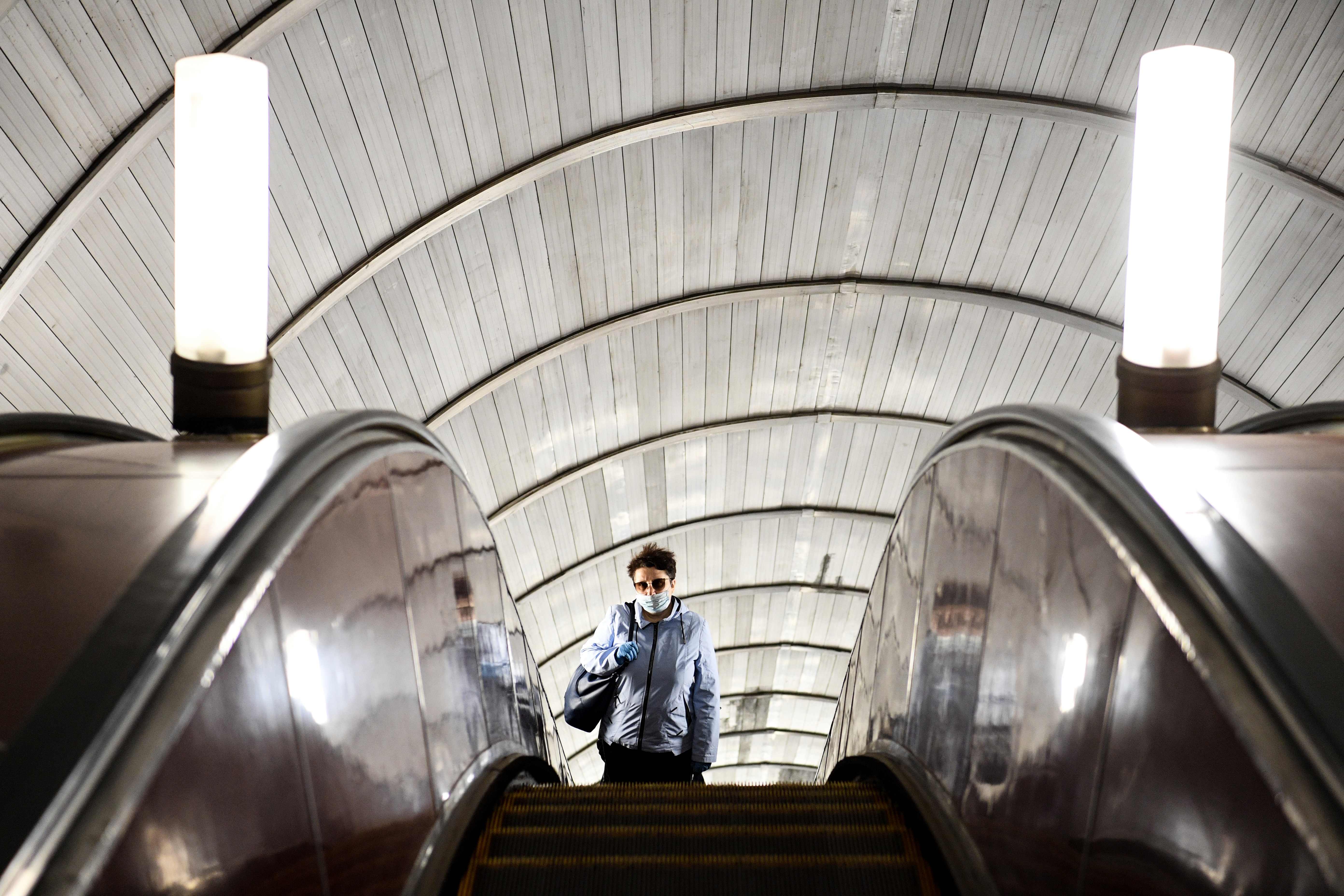 Seorang penumpang mengenakan masker dan sarung tangan naik eskalator di Stasiun Savyolovskaya, Moskow, Rusia.