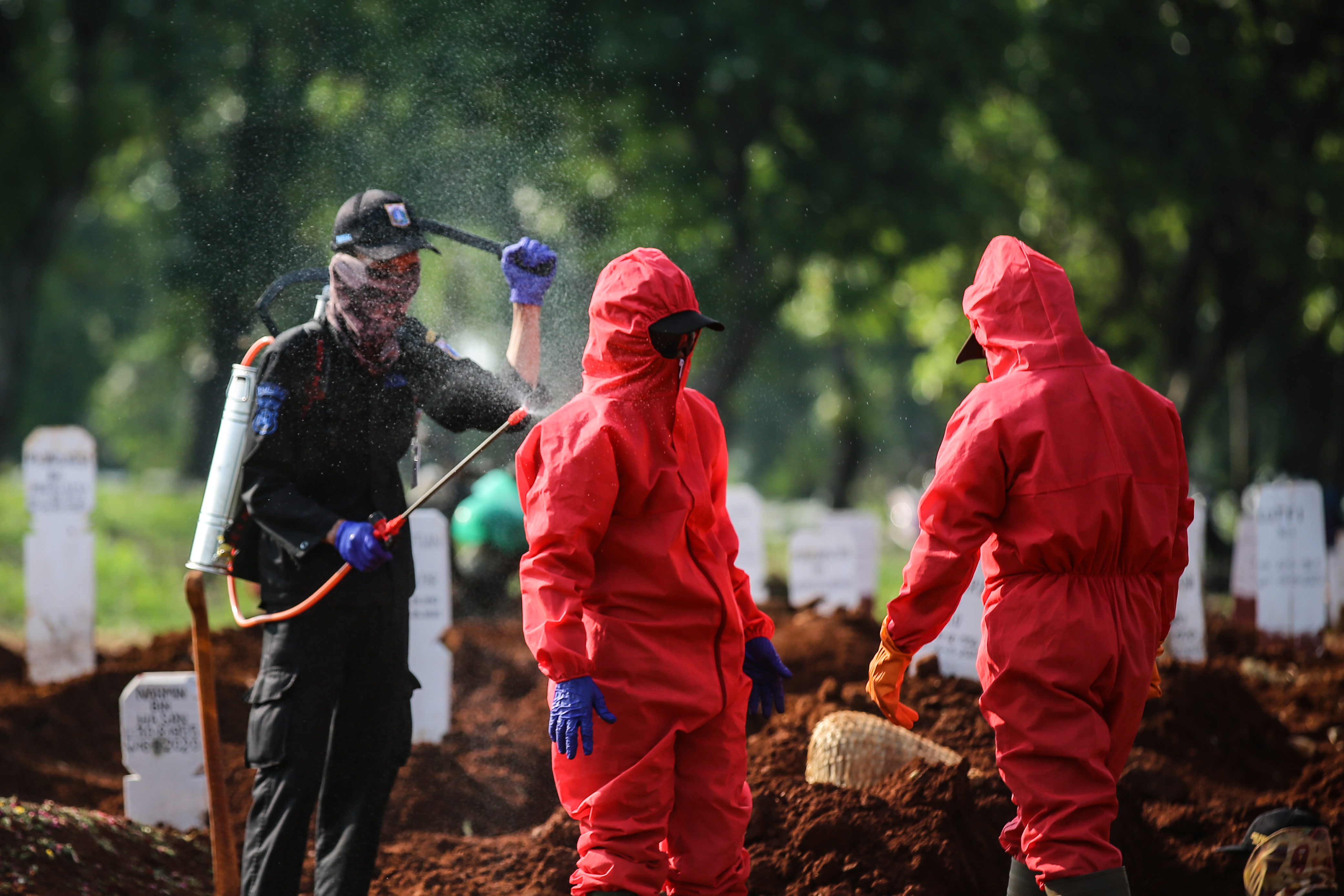 Petugas pemakaman disemprot cairan disinfektan seusai memakamkan jenazah covid-19 di TPU Pondok Ranggon, Kamis (7/5). 