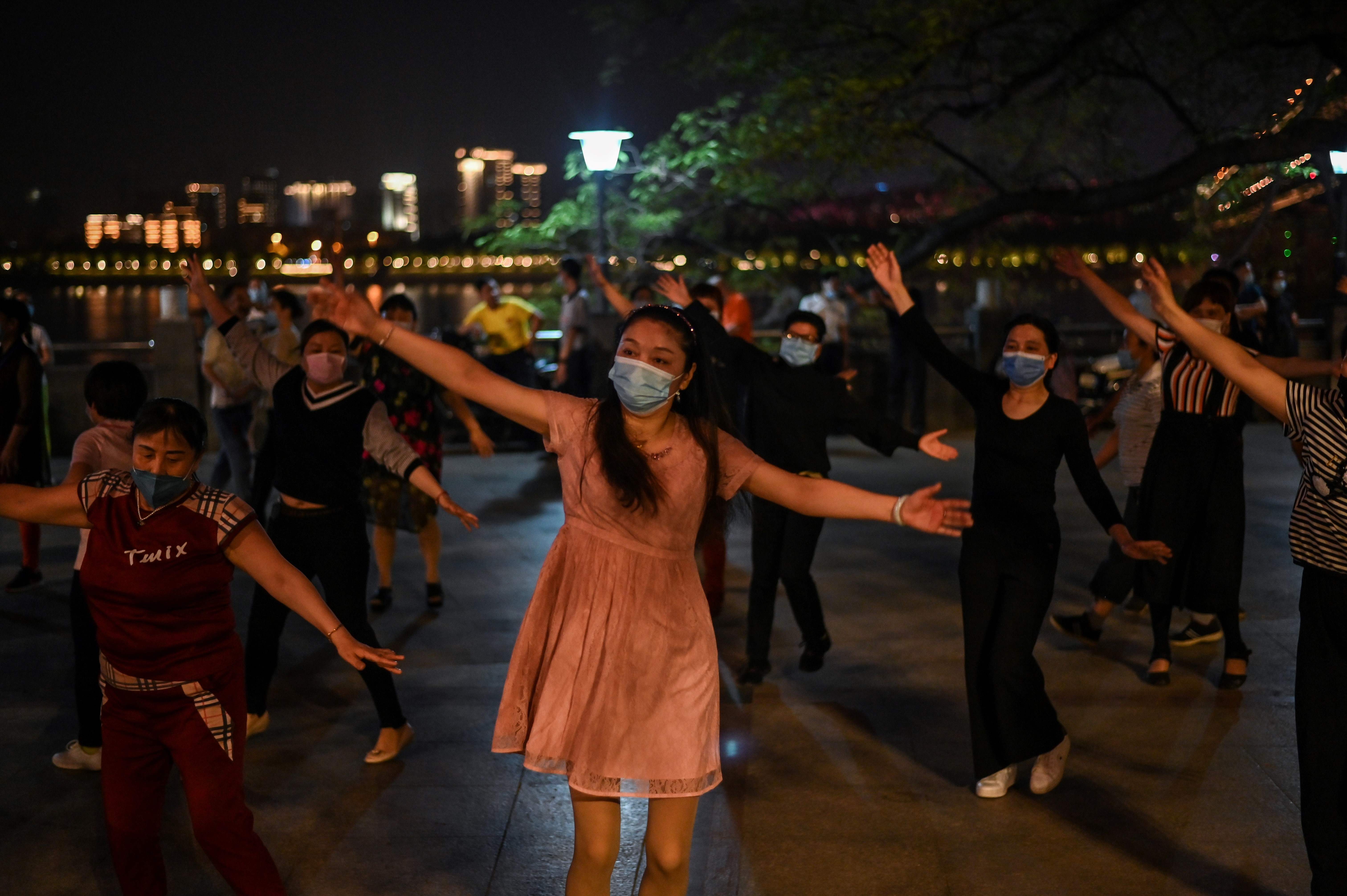 Sekelompok orang mengenakan masker menari di tepi Sungai Yangtze, Wuhan, Tiongkok.