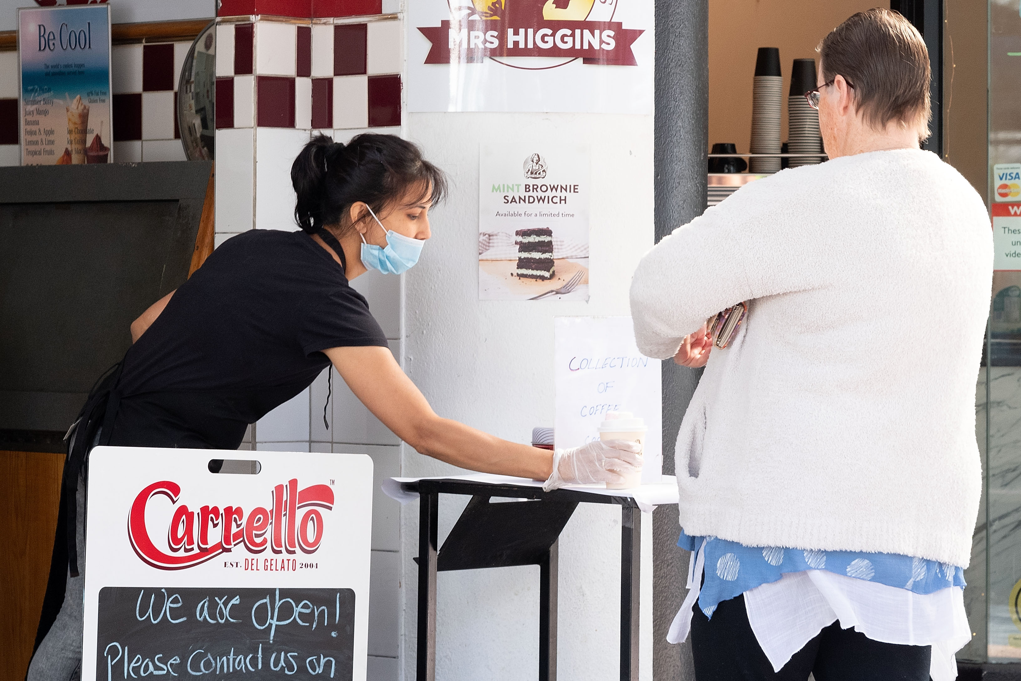 Seorang wanita (menerima pesanannya di luar sebuah toko kecil pada hari pertama pelonggaran pembatasan di Wellington, Selasa (28/4).