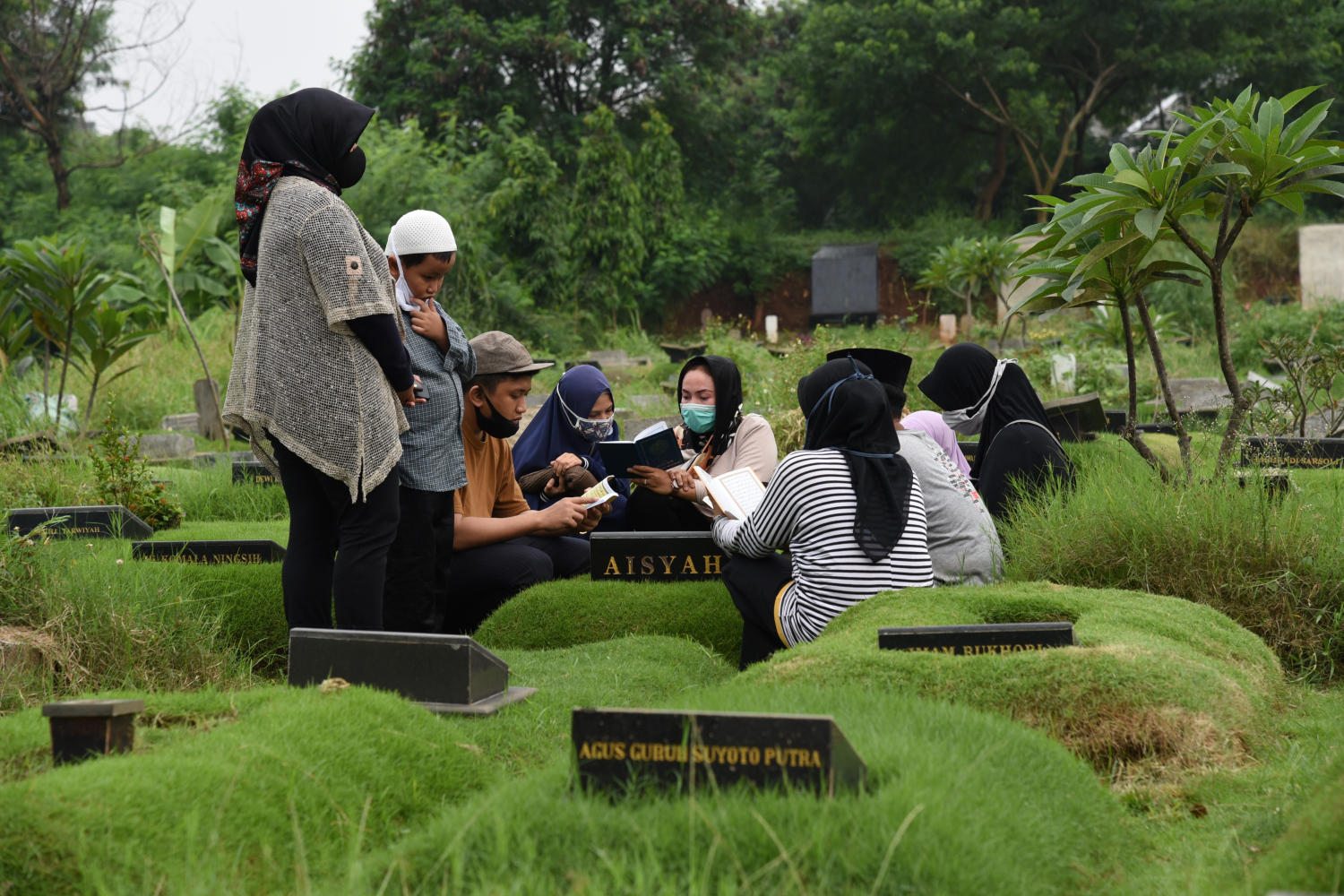 Peziarah mengenakan masker pelindung tengah berdoa di depan makam di TPU Tanah Kusir, Jakarta
