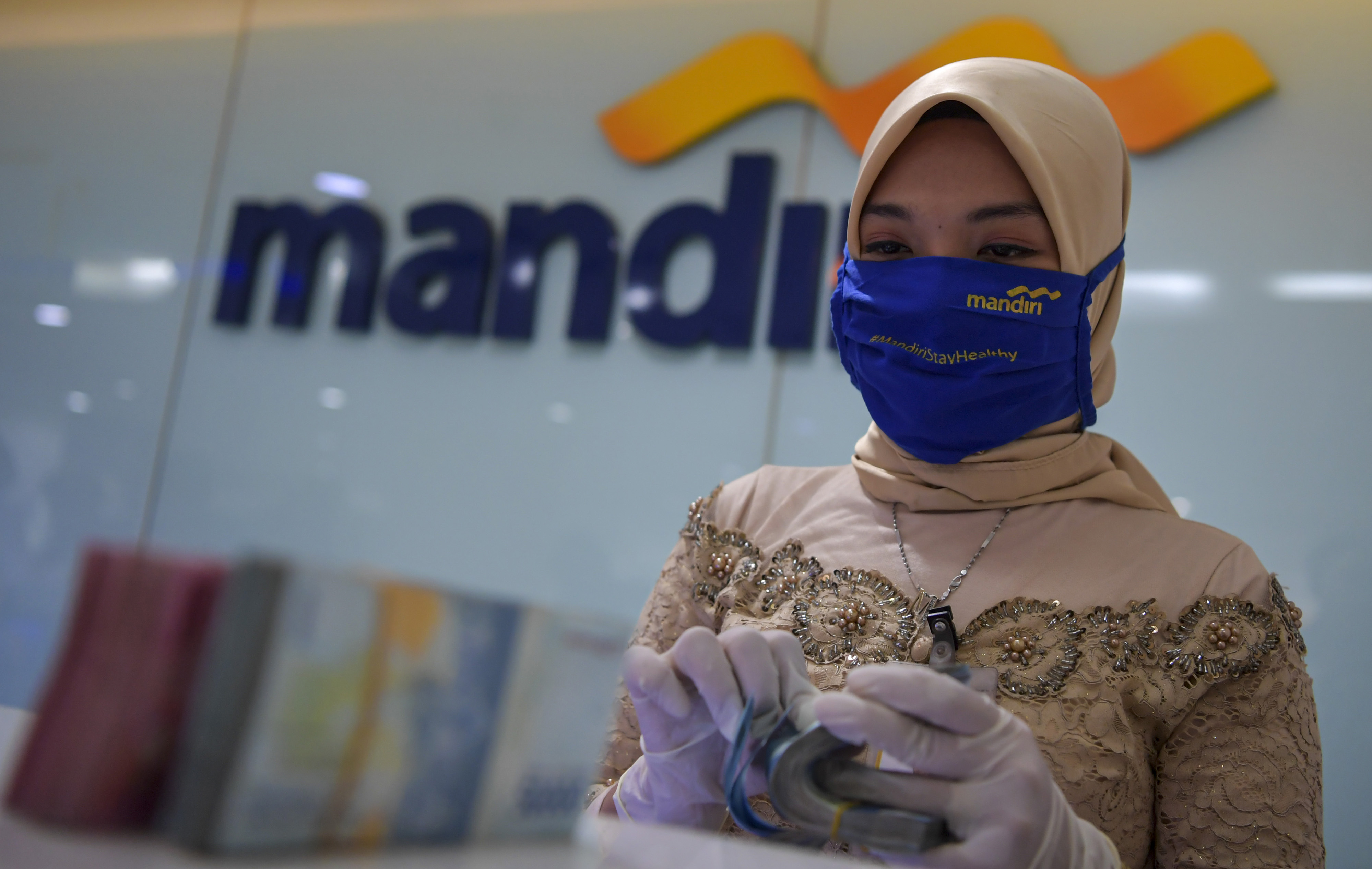  Karyawan Bank Mandiri mengenakan pakaian adat kebaya menghitung uang saat melayani nasabah di kantor cabang di Jatinegara, Jakarta.