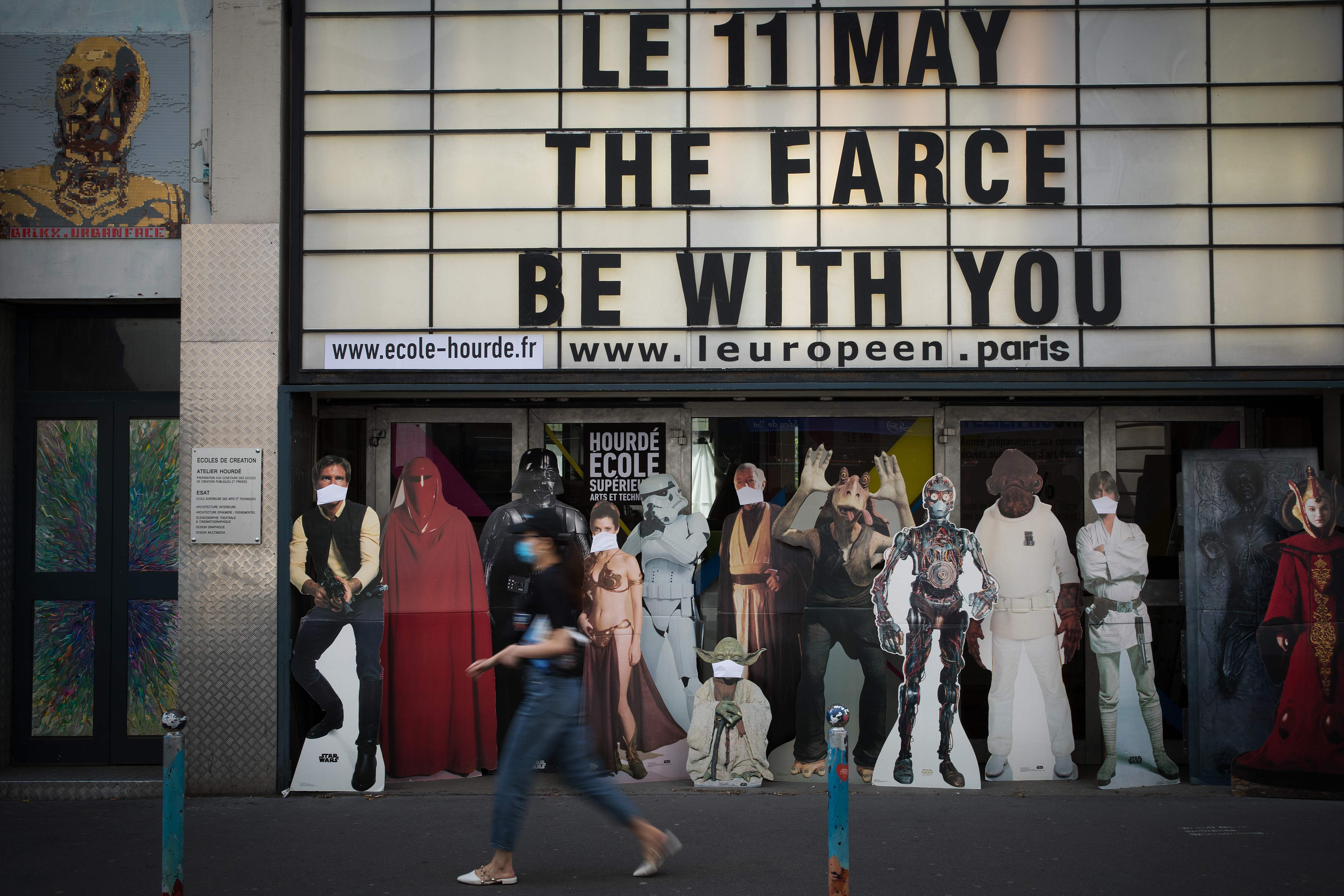 Seorang warga berjalan di depan cutboard cutout karakter Star Wars yang dipakaikan masker di Paris, Prancis.