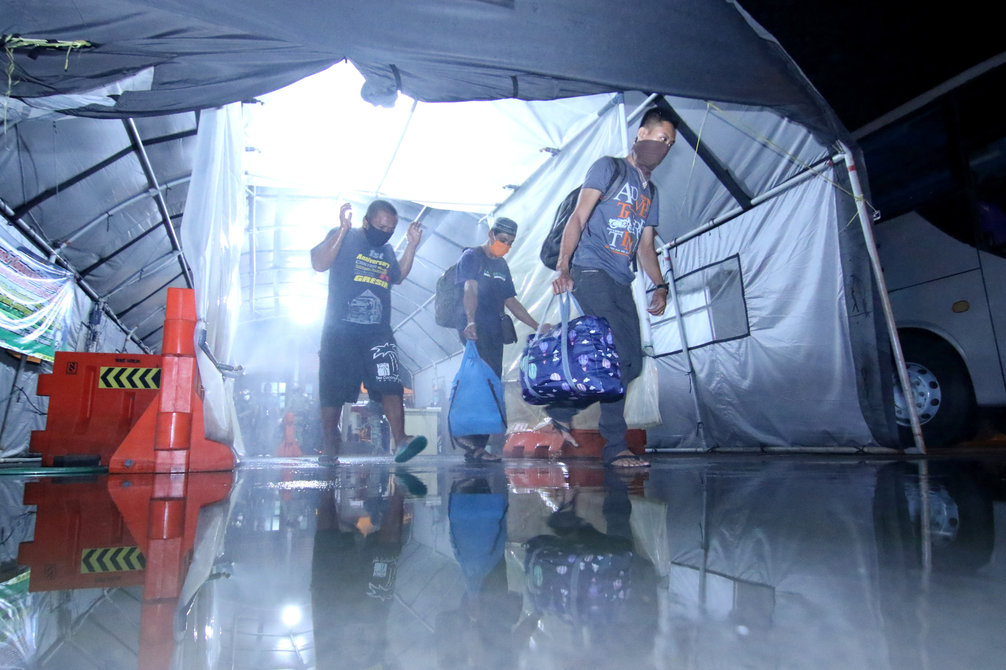 Pemudik asal Bali melintasi semprotan cairan disinfektan usai melakukan pemeriksaan dan pendataan di Pelabuhan Ketapang Banyuwangi.