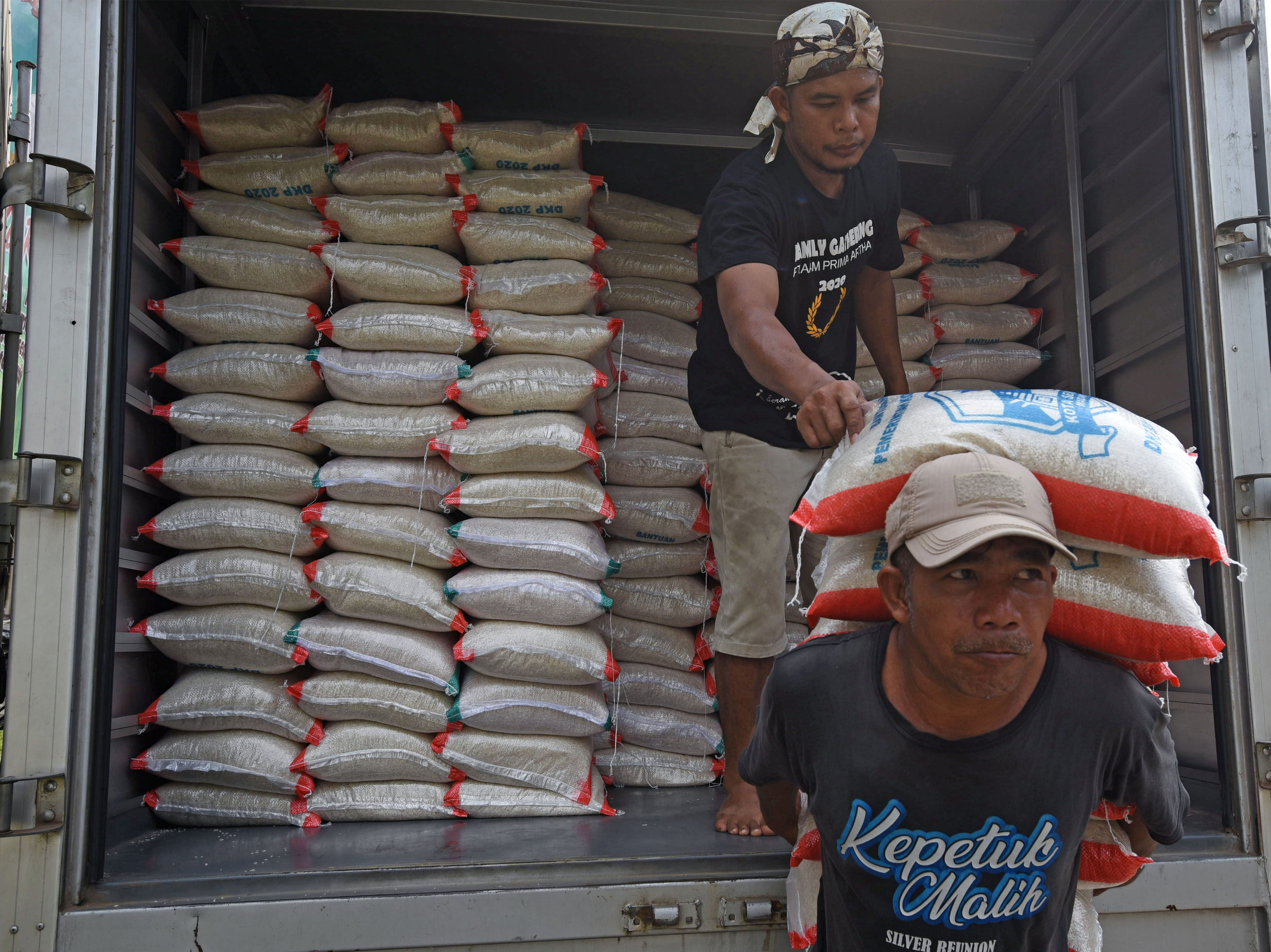 Pekerja menurunkan beras bantuan untuk warga terdampak pandemi.