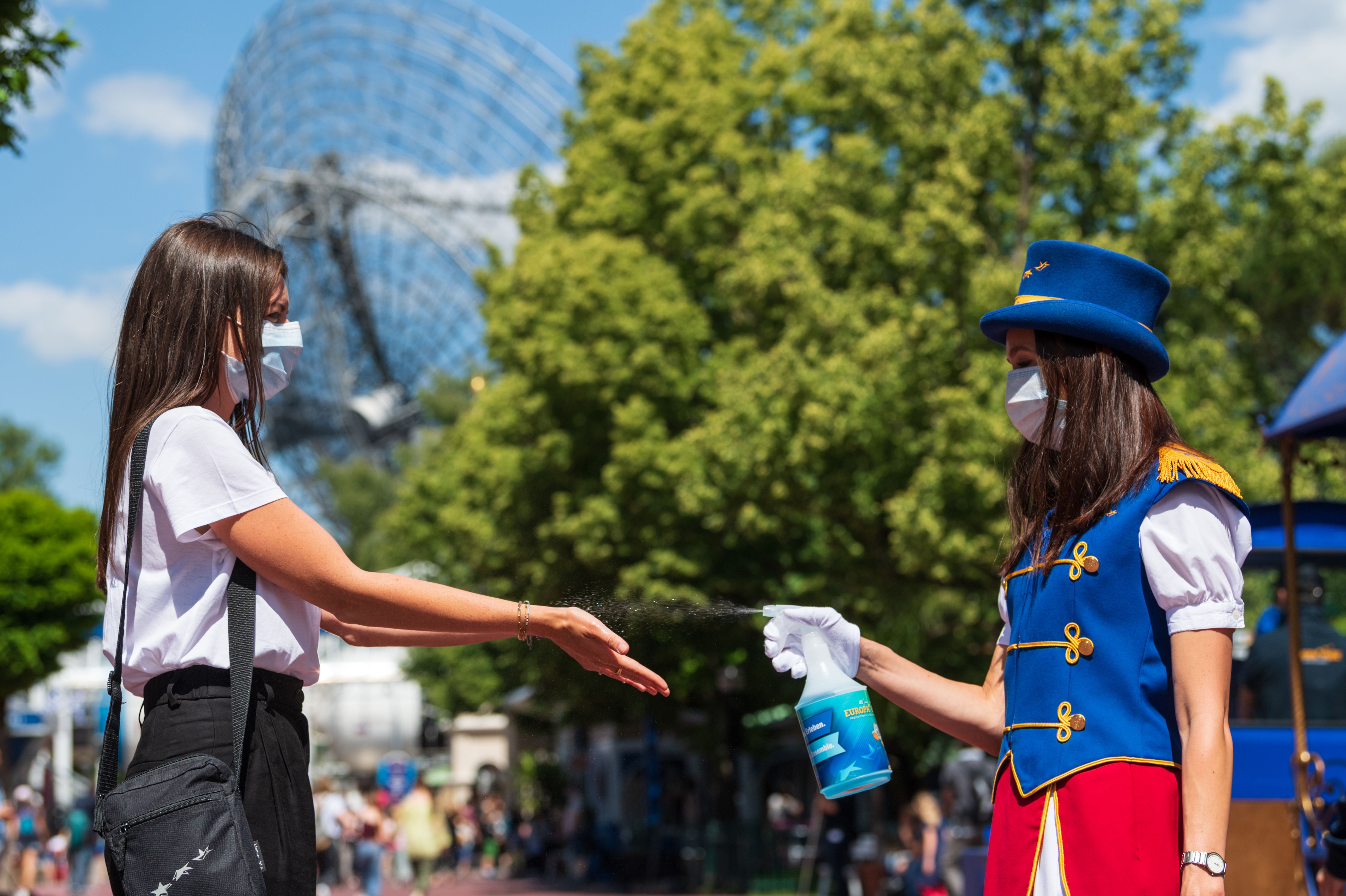 Seorang karyawan mengenakan masker dan menyemprotkan cairan disinfektan ke pelanggan di taman hiburan di Jerman, Jumat (29/5)