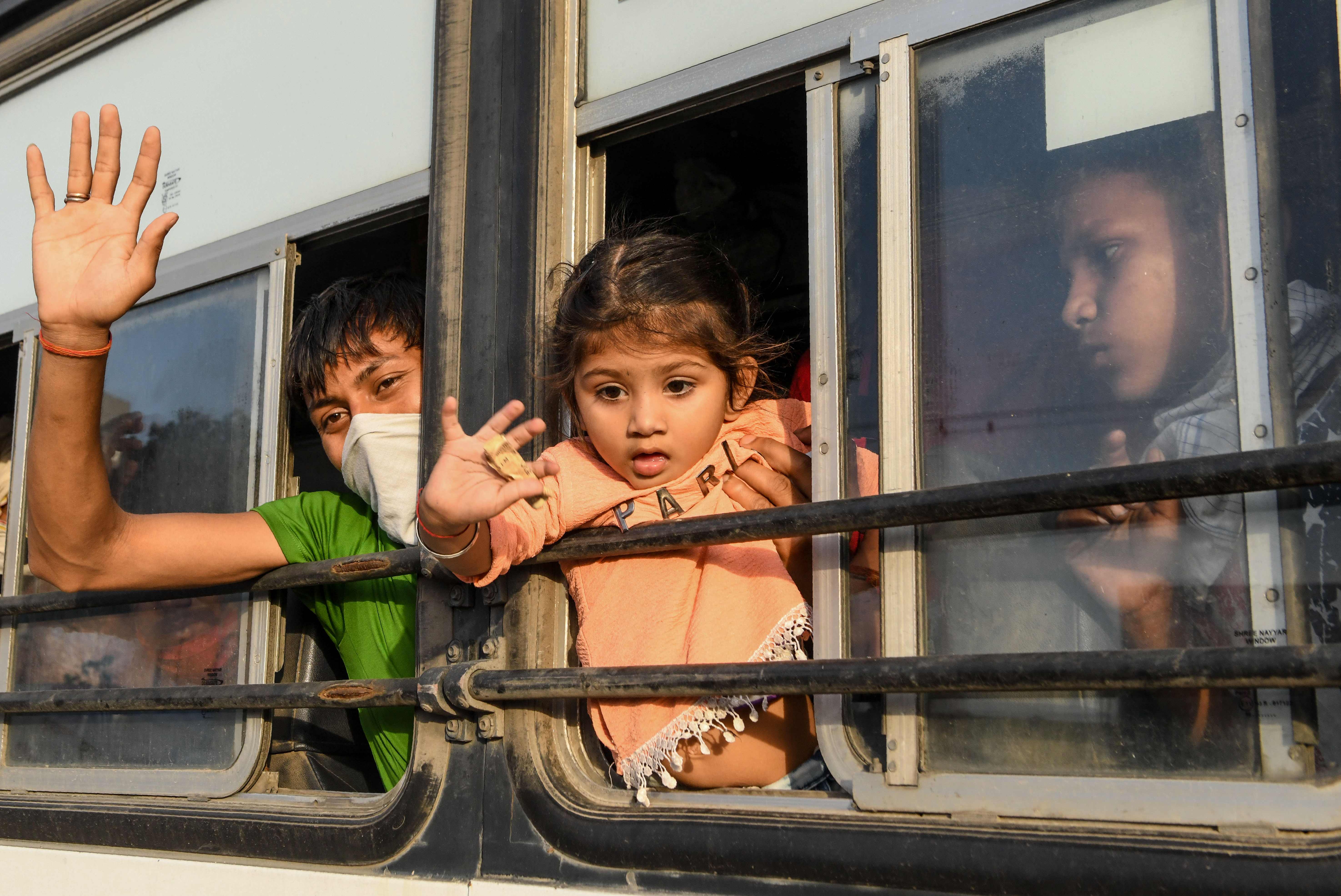 Pekerja migran dan keluarga dari Gonda di negara bagian Uttar Pradesh melambai dari jendela bus ketika mereka tiba di stasiun kereta api.