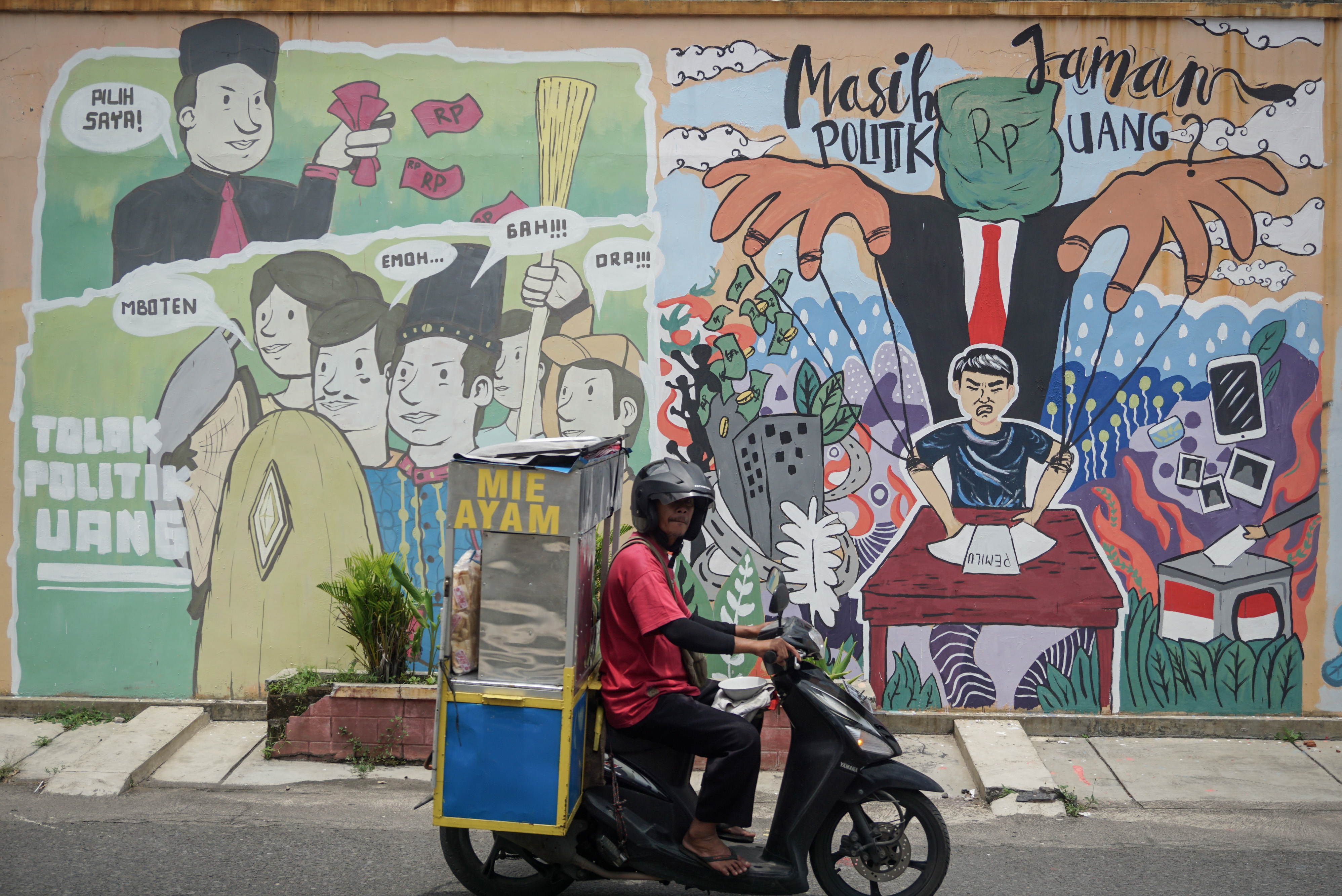 Pengendara motor melintasi mural bertema anti politik uang di Kampung Sondakan, Solo, Jawa Tengah.