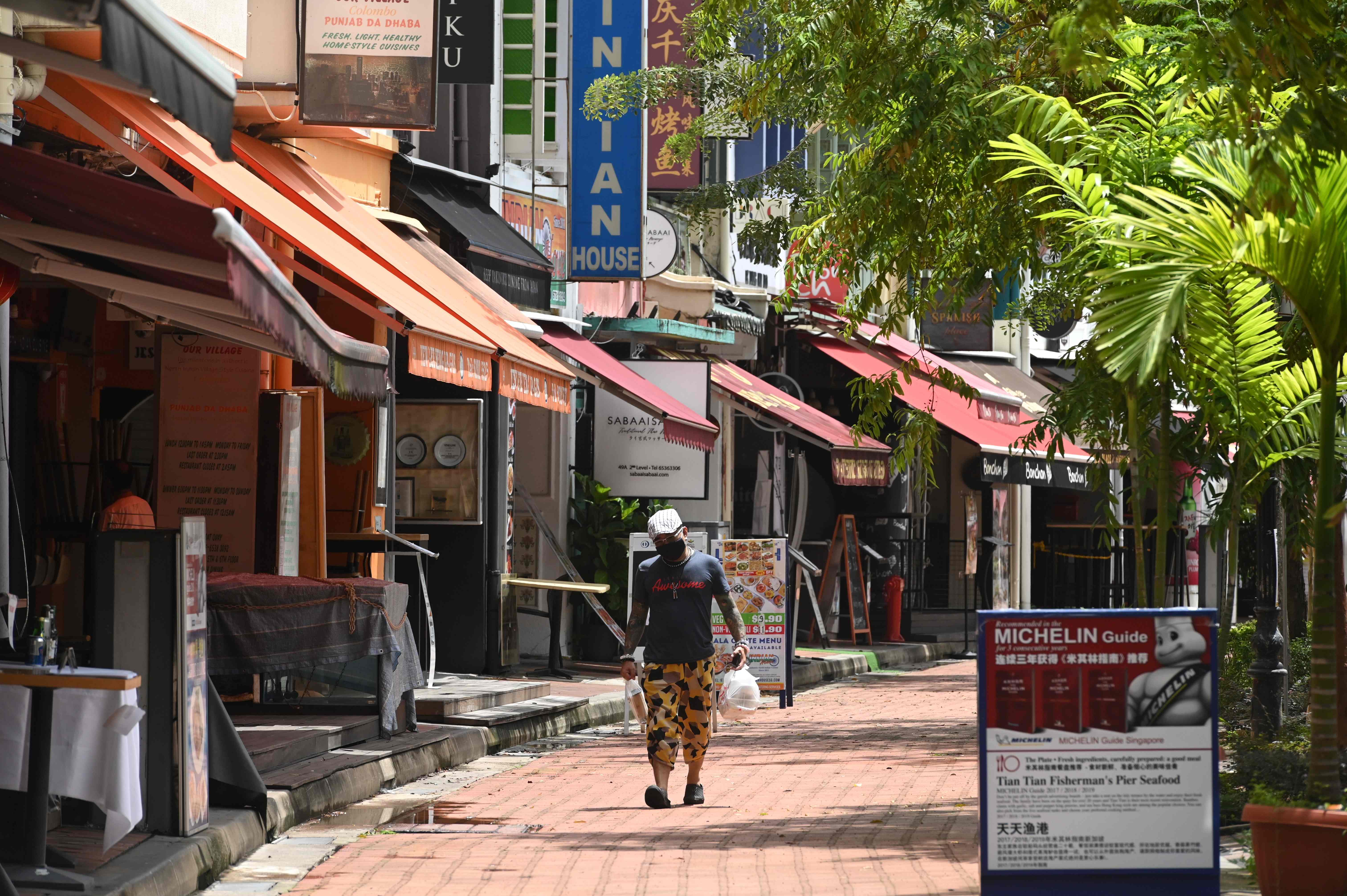 Seorang pria mengenakan masker membawa makanan untuk dibawa pulang berjalan di lorong restoran di Singapura, Senin (11/5).