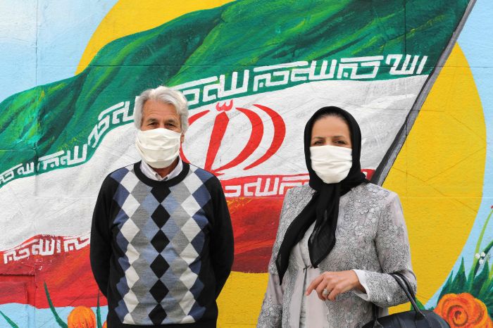 Dua warga Iran memakai masker berpose di depan lukisan bendera Iran di Teheran (13/4)