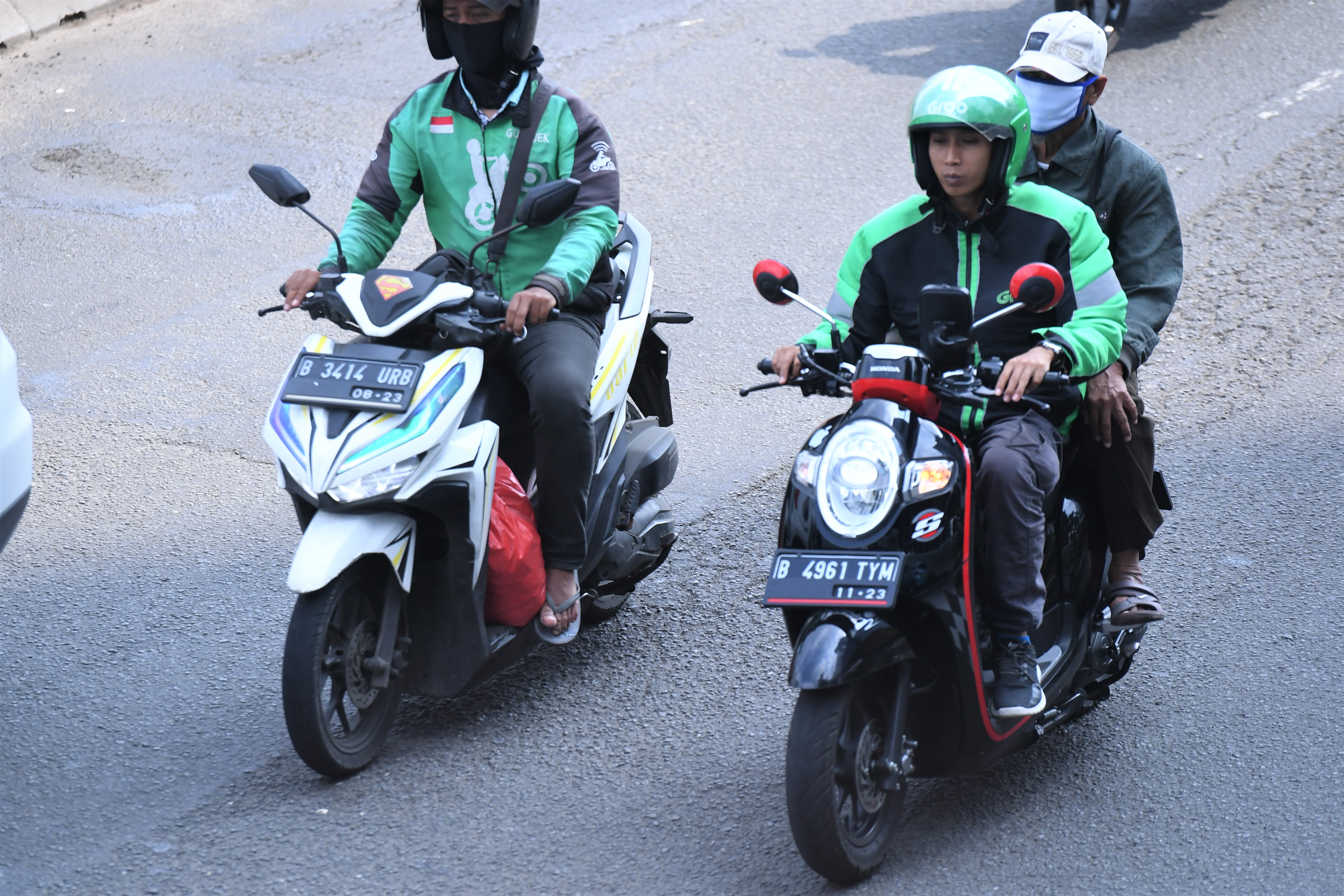 Pengemudi ojek online tidak menggunakan masker dan mengangkut penumpang saat melintas di Jalan MT Haryono, Jakarta, hari ini.