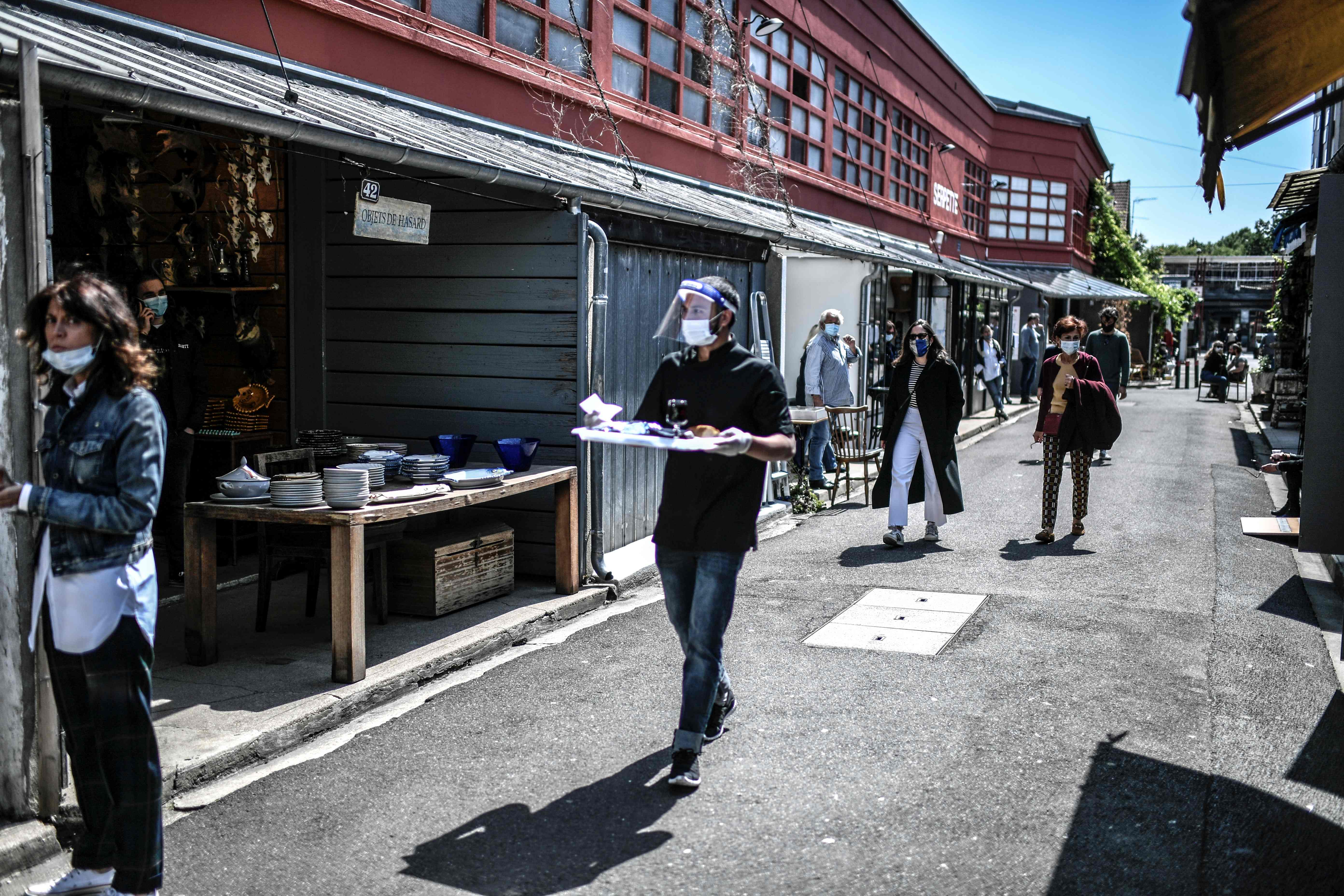 Seorang pelayan mengenakan masker dan faceshield mengantarkan makanan di sebuah pasar loak di Paris, Prancis.