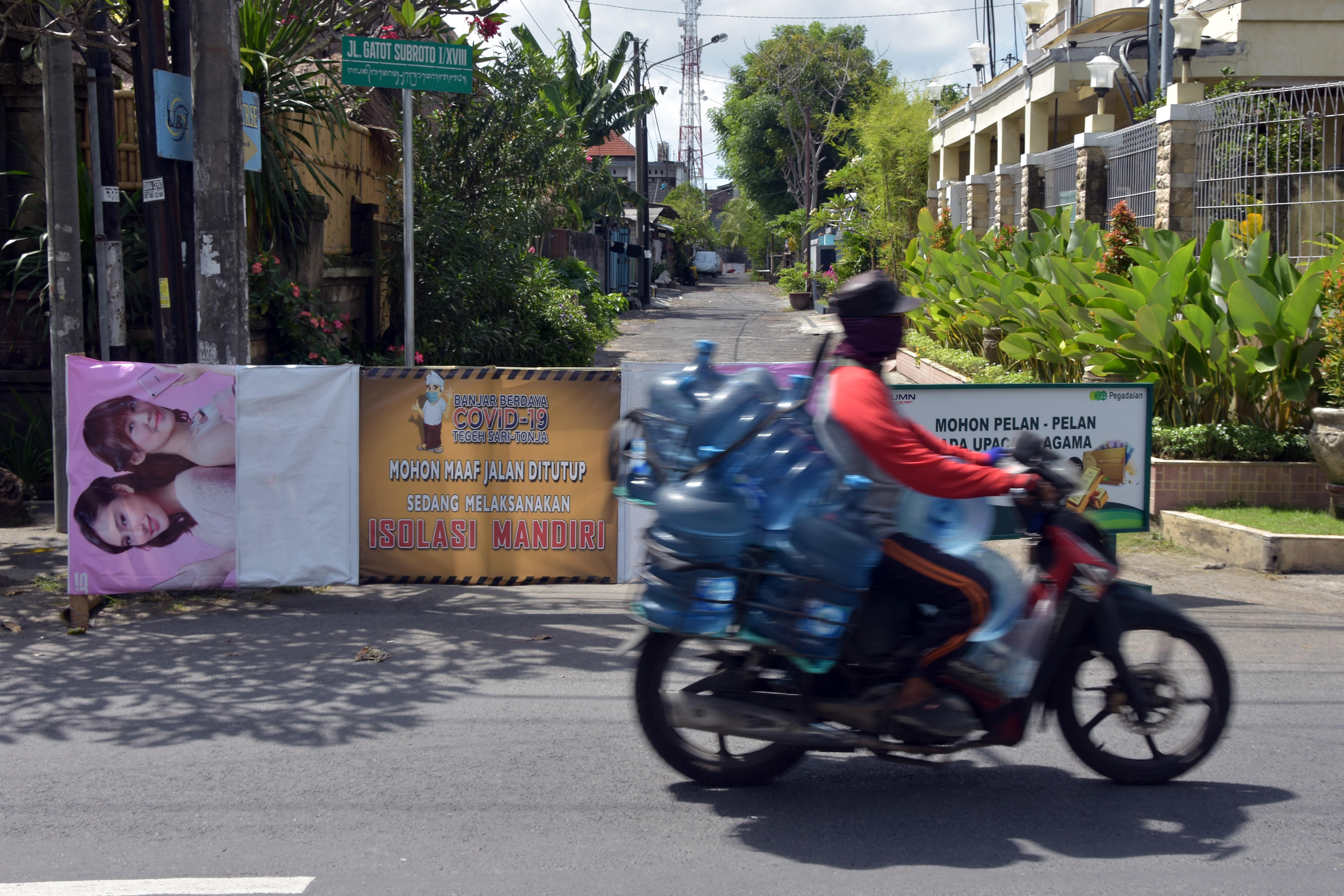 Pengendara motor melintas di dekat jalan perumahahan yang ditutup karena warganya melakukan isolasi mandiri di Denpasar, Bali.