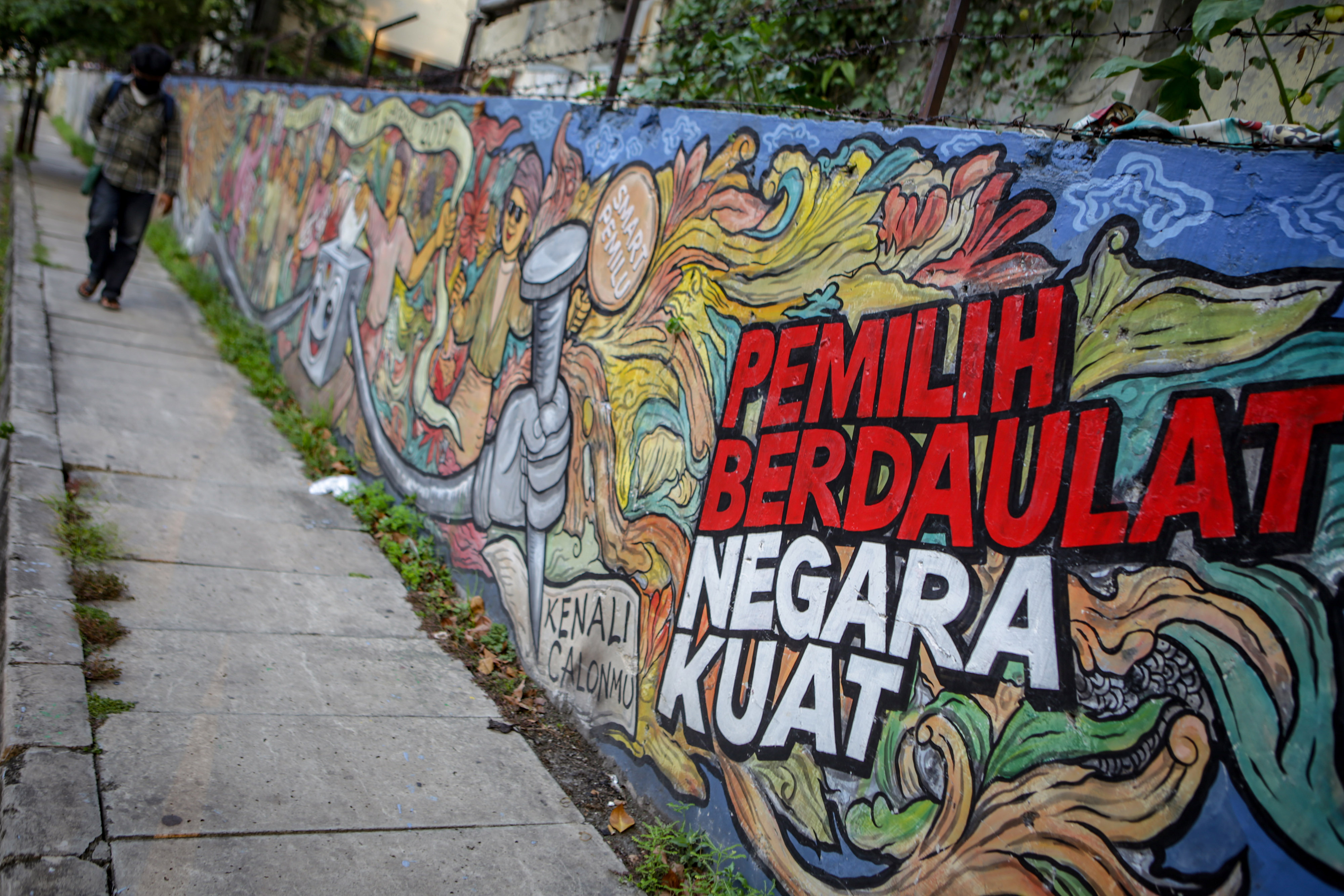 Warga melintasi mural bertema pemilu di wilayah Kota Tangerang, Banten.