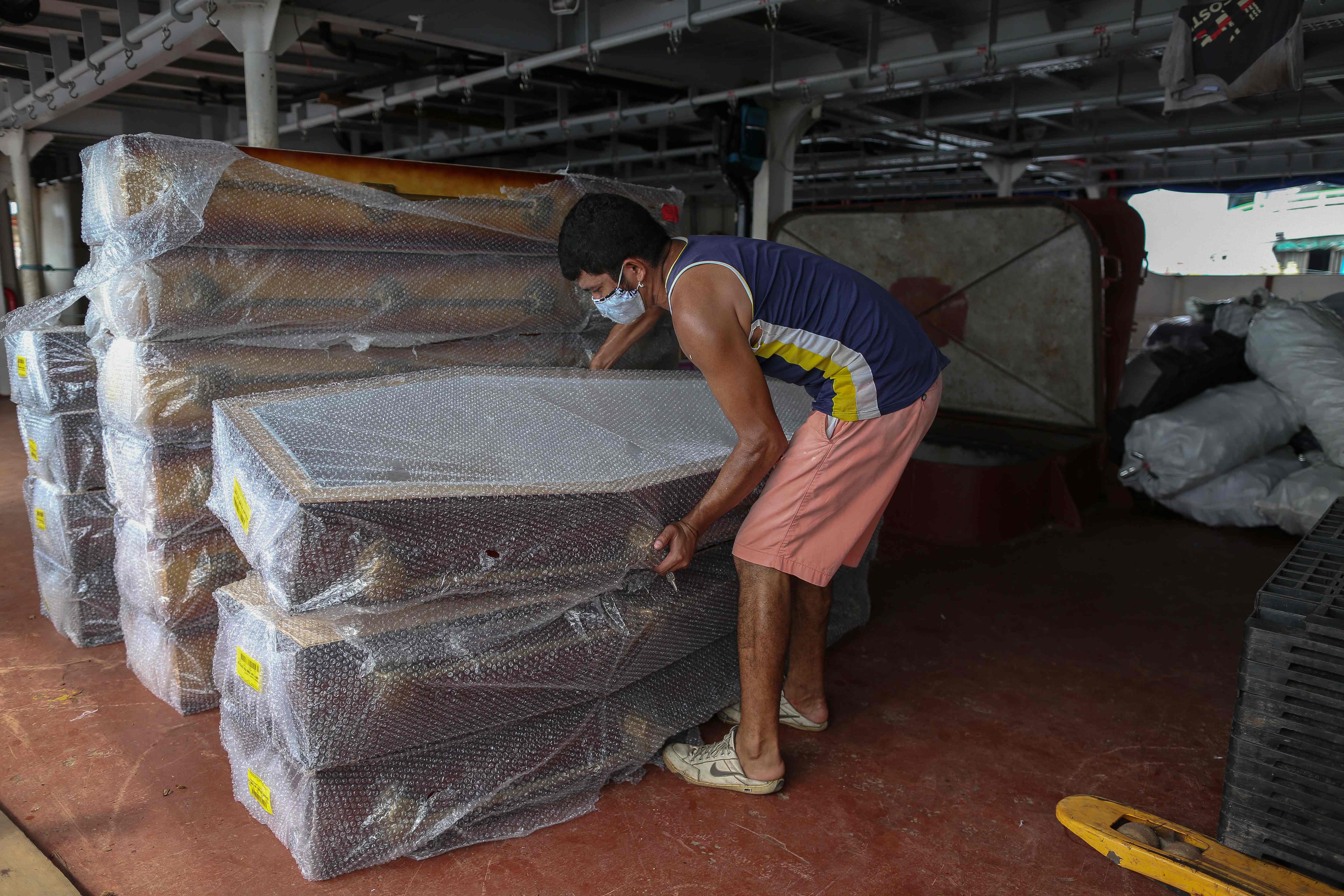 Seorang pekerja menurunkan peti jenazah dari kapal di Manaus, Brasil, seiring meningkatkanya permintaan akibat covid-19.