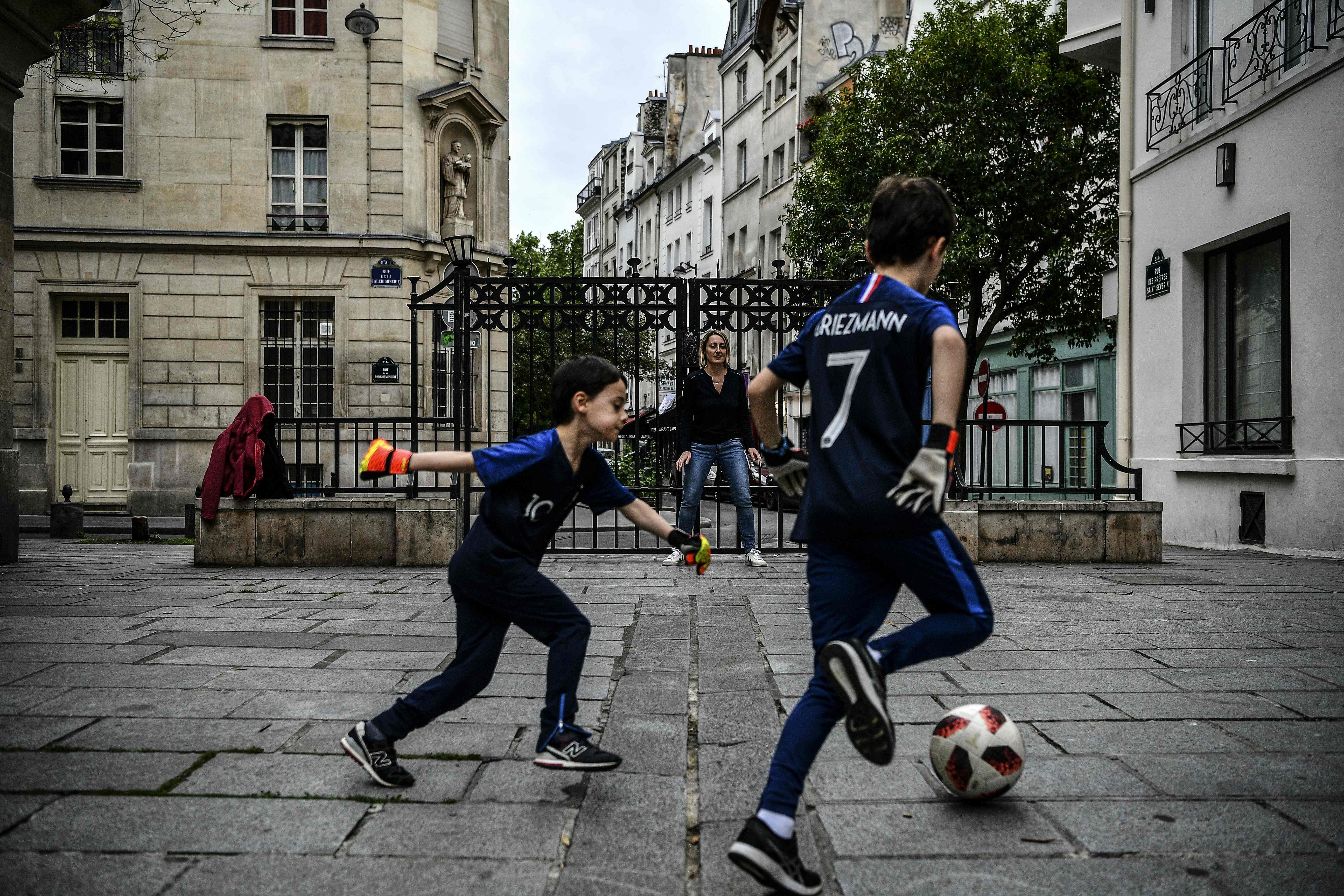 Seorang wanita dan anak-anaknya bermain sepak bola di lapangan yang sepi di Paris, Senin (4/5), pada hari ke-49 lockdown di Prancis. 