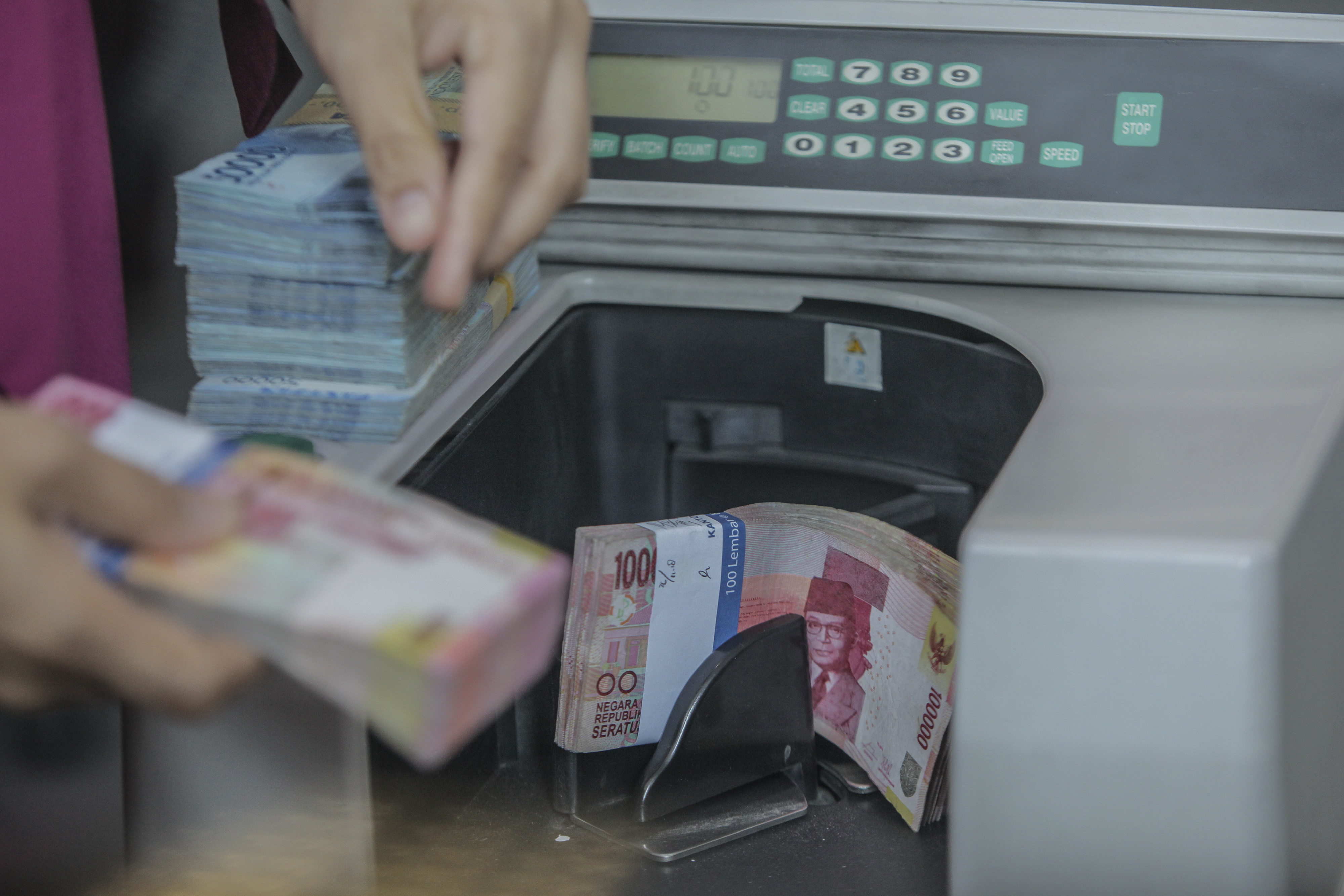Petugas gerai penukaran valuta asing menghitung uang rupiah dengan mesin khusus.