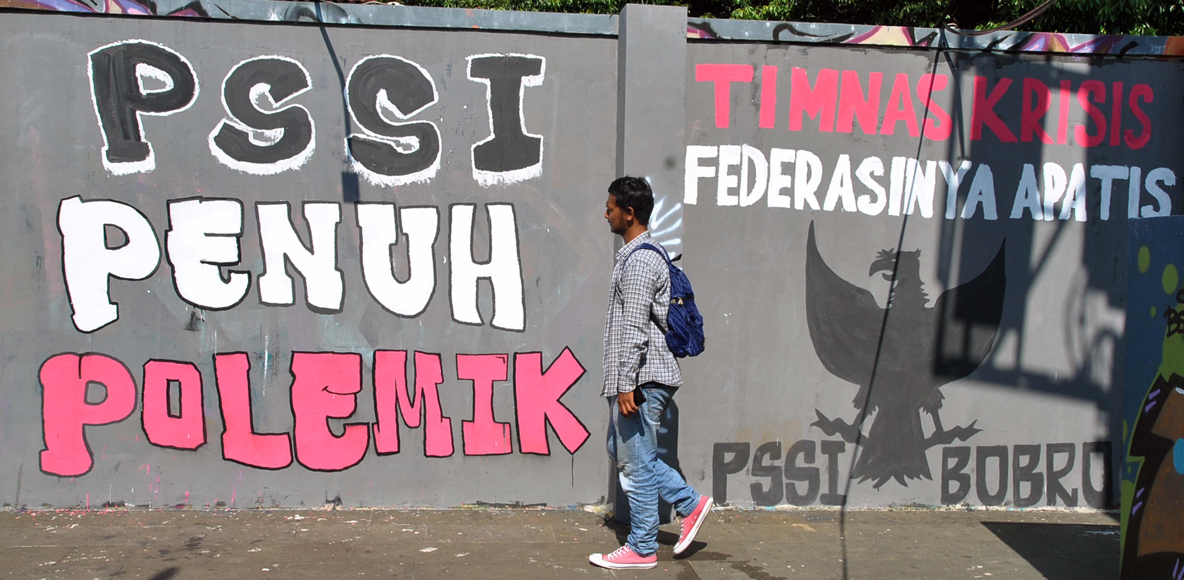 Warga berjalan melewati mural bergambar burung Garuda dan tulisan Persatuan Sepakbola Seluruh Indonesia (PSSI)