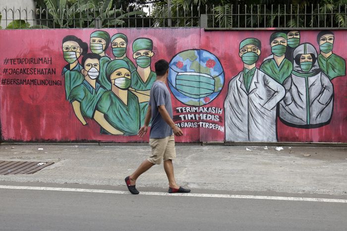 Warga melintas di depan mural tentang pandemi virus korona di Jalan Raya Jakarta-Bogor, Depok, Jawa Barat, Minggu (5/4).