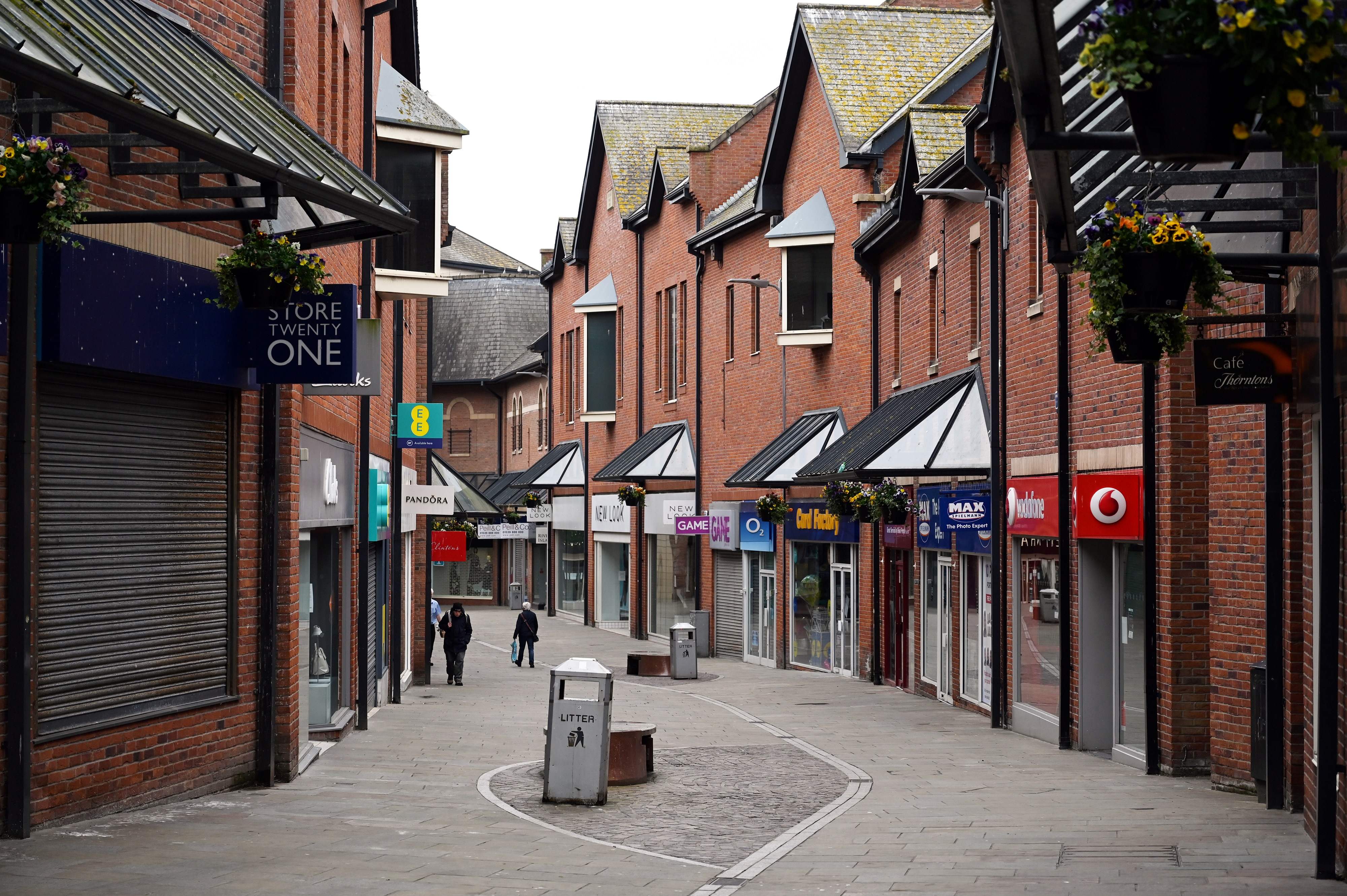 Warga melintas di depan toko-toko yang kosong di Barrow-in-Furness, Inggris akibat pandemi covid-19.