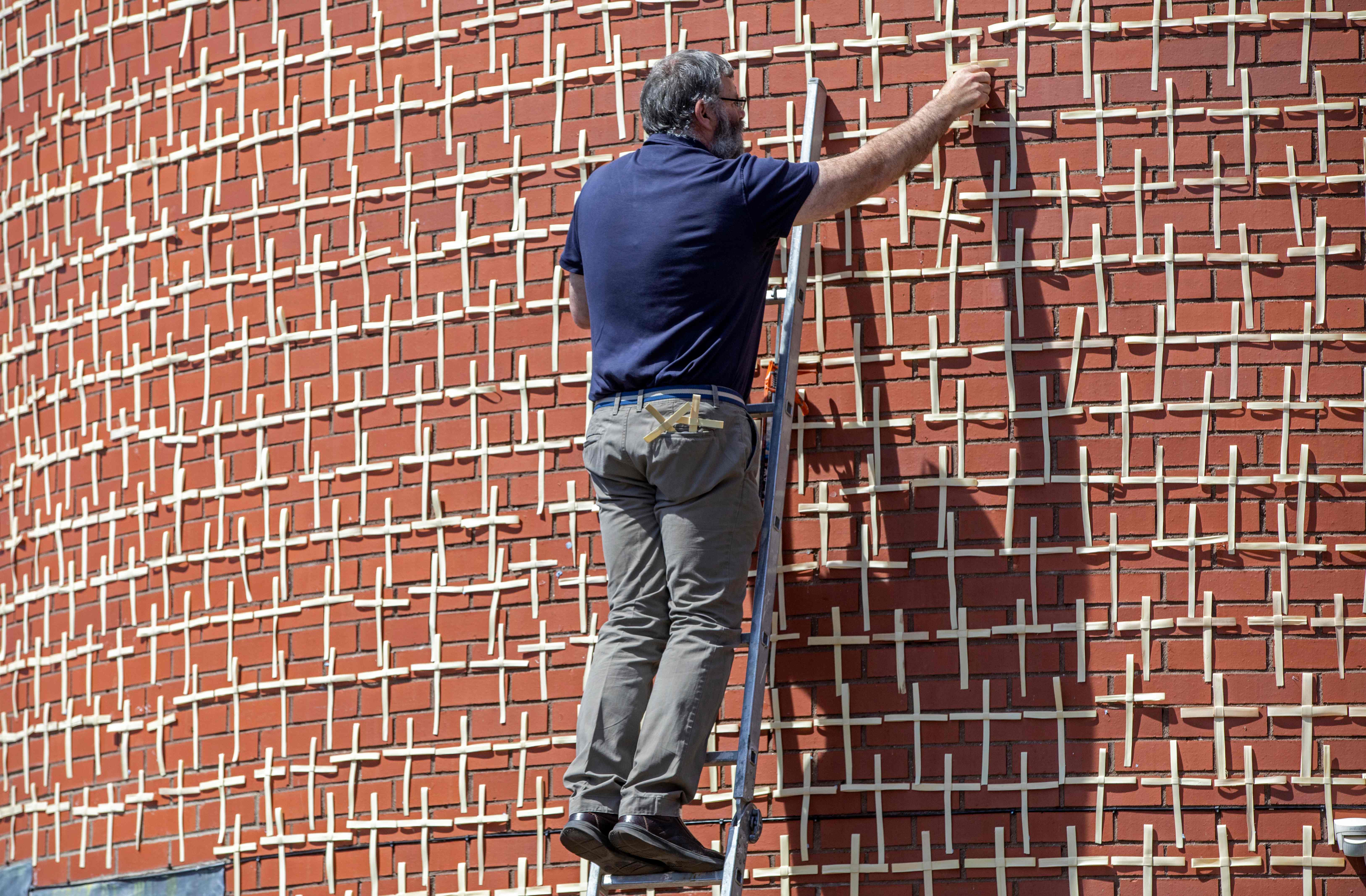 Petugas menambahkan salib di antara 2 ribu salib yang dipasang di sebuah gereja di Dublin, Irlandia. Salib itu melambangkan korban covid-19.