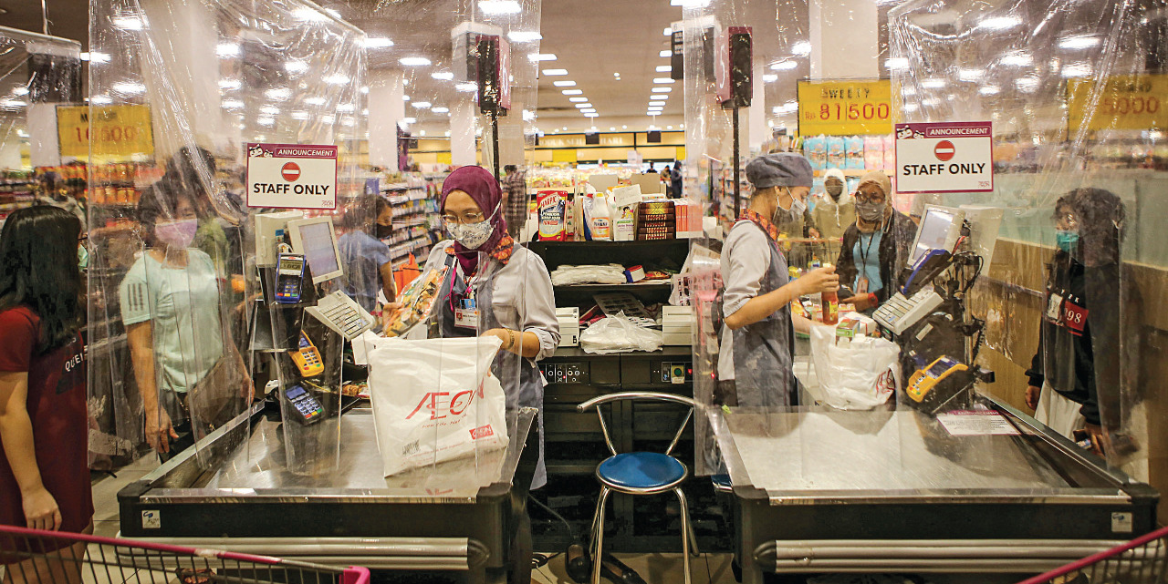 Petugas kasir melayani konsumen dari balik sekat plastik.