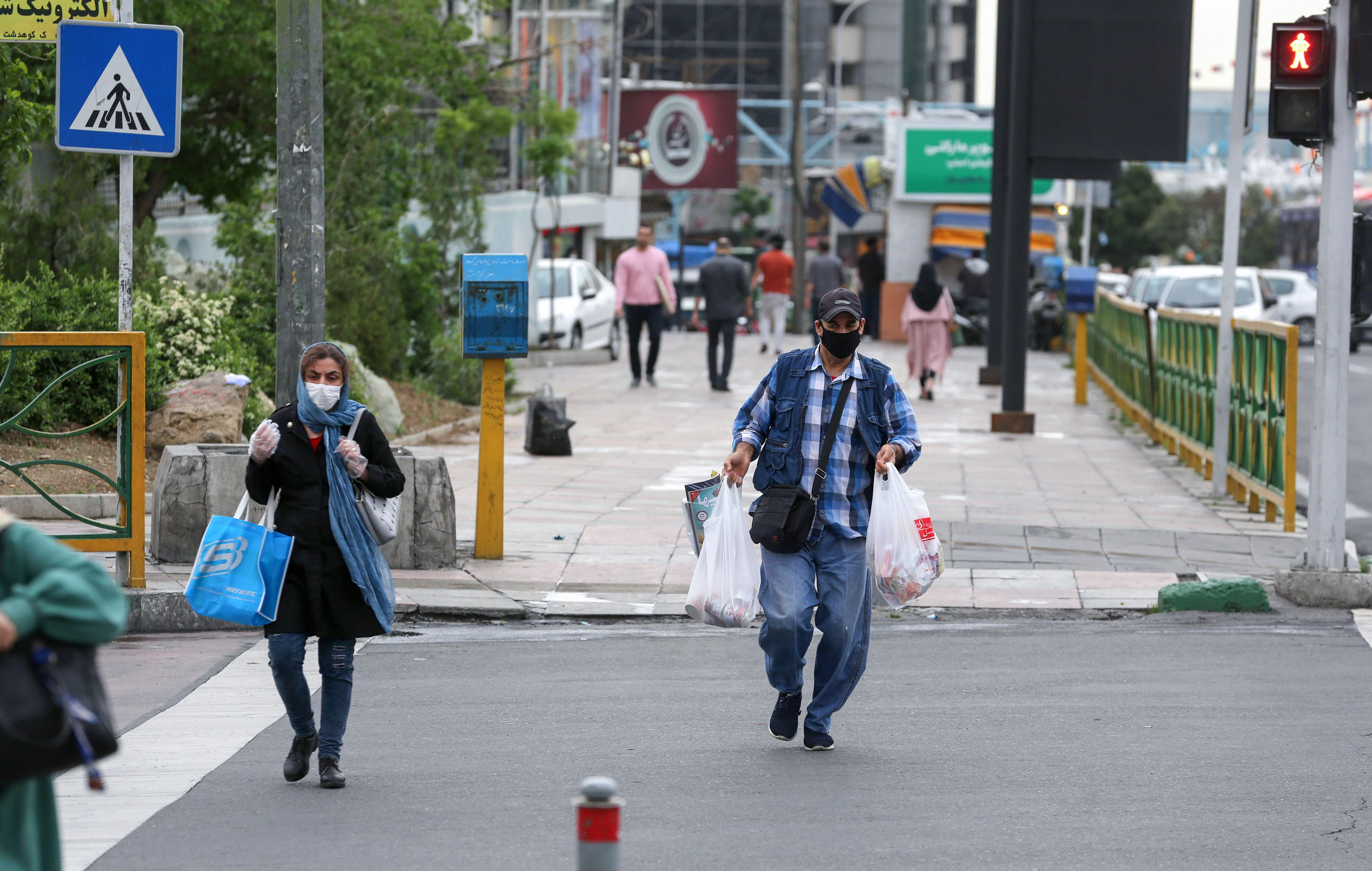 Penduduk Iran mengenakan masker saat menyeberang jalan di Teheran pada 26 April 2020. Hal itu dilakukan untuk mencegah penularan covid-19.