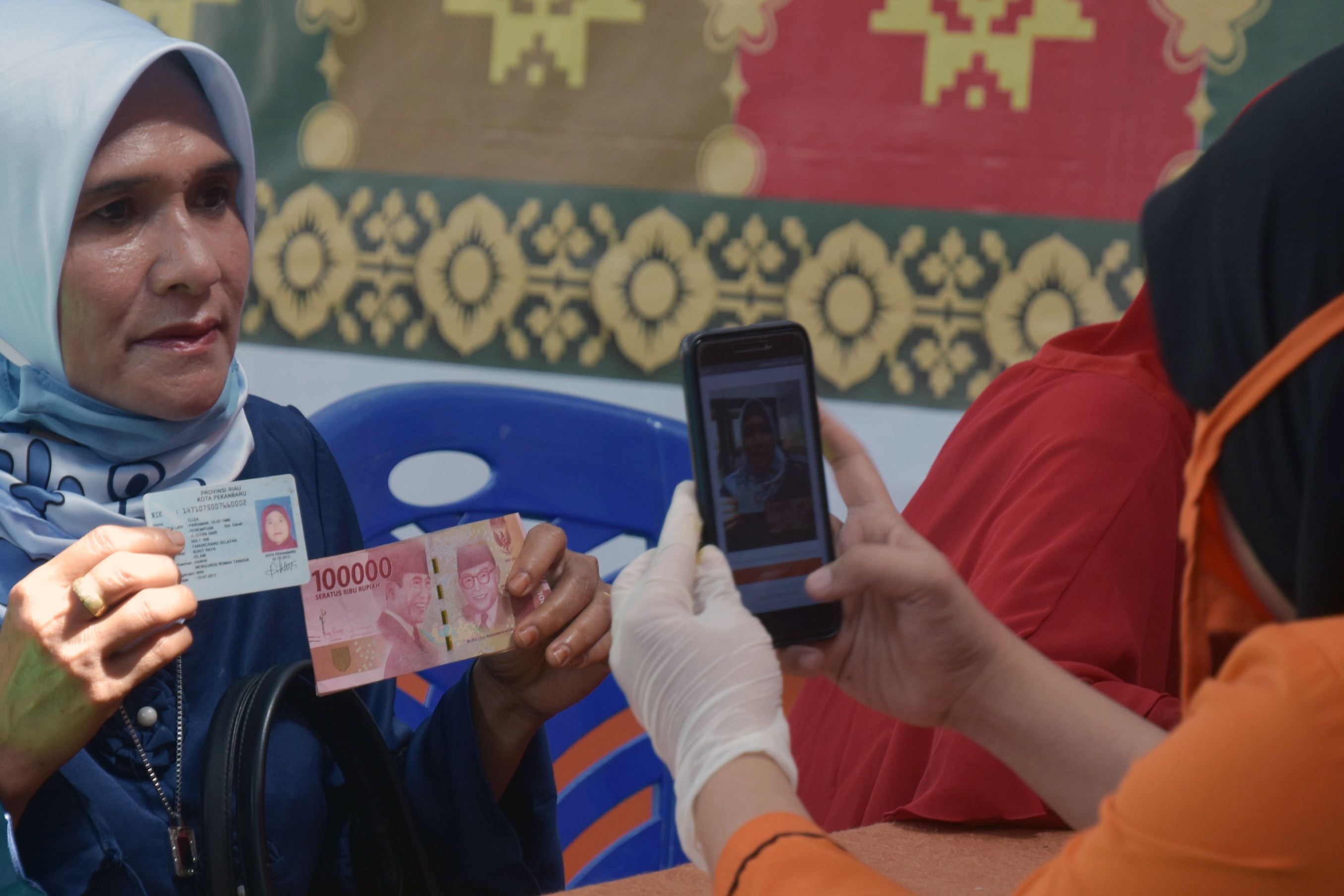 Petugas memotret warga saat serah terima dana bantuan sosial (Bansos) tunai di Kota Pekanbaru, Riau, Jumat (8/5). 