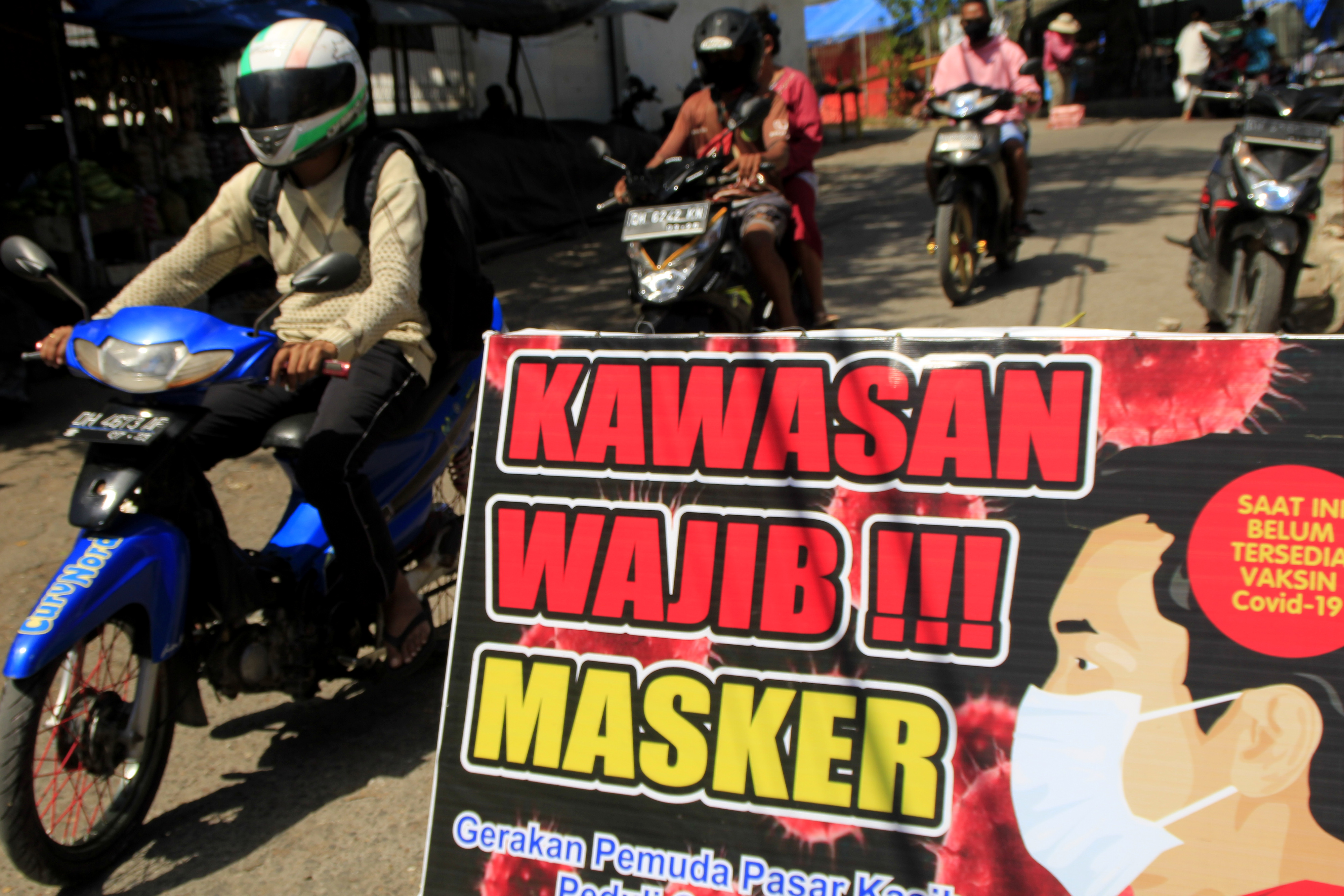 Pengendara bermotor melintas di samping tulisan kawasan wajib masker di pintu masuk pasar Kasih Naikoten, Kota Kupang, NTT, Kamis (14/5)