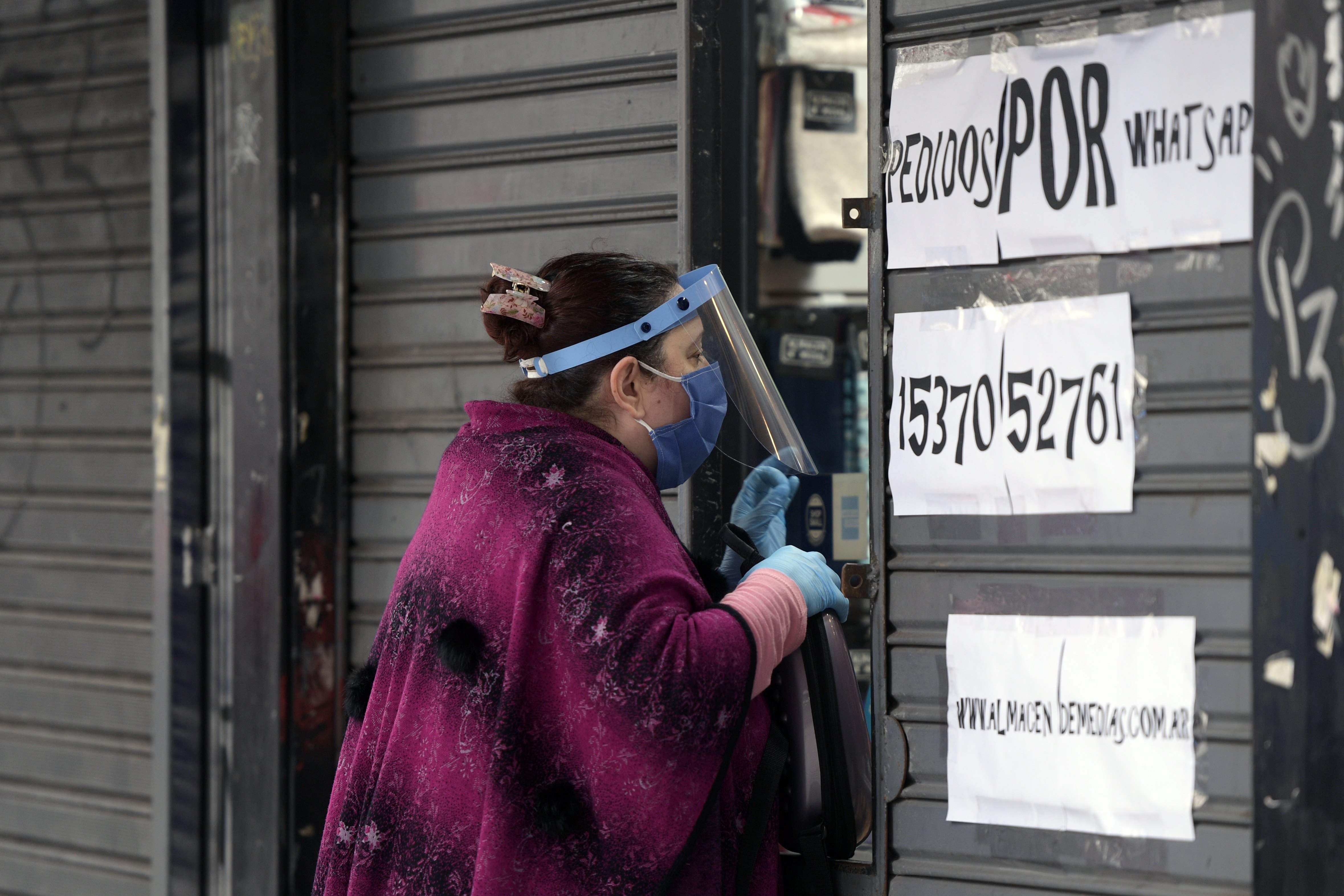 Seorang perempuan di Argentina mengenakan pelindung wajah, sarung tangan dan masker saat mengambil pesanan