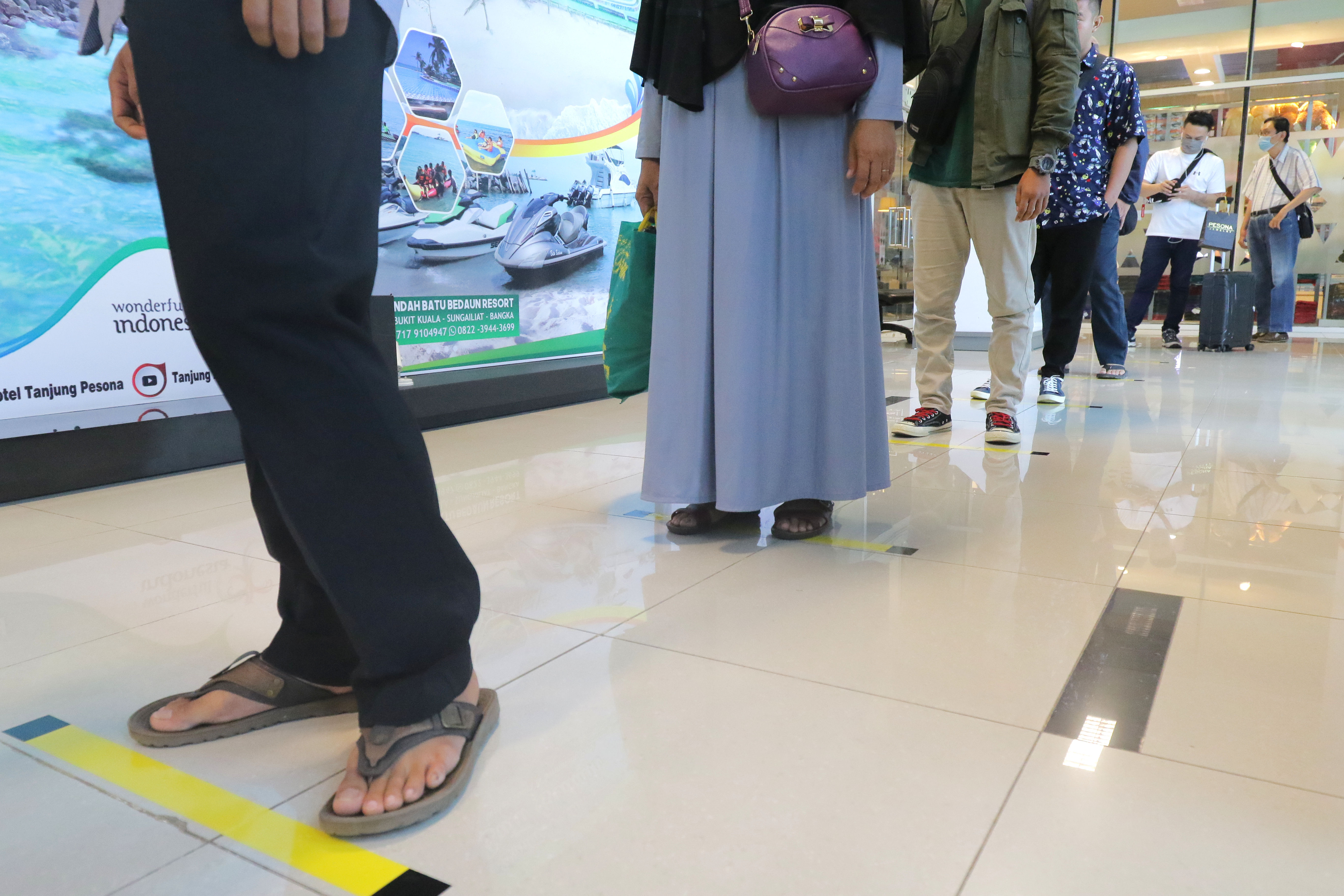 Penumpang mengantre di lantai yang telah diberi stiker panduan jarak di Bandara Depati Amir, Kota Pangkalpinang, Kepulauan Bangka Belitung.