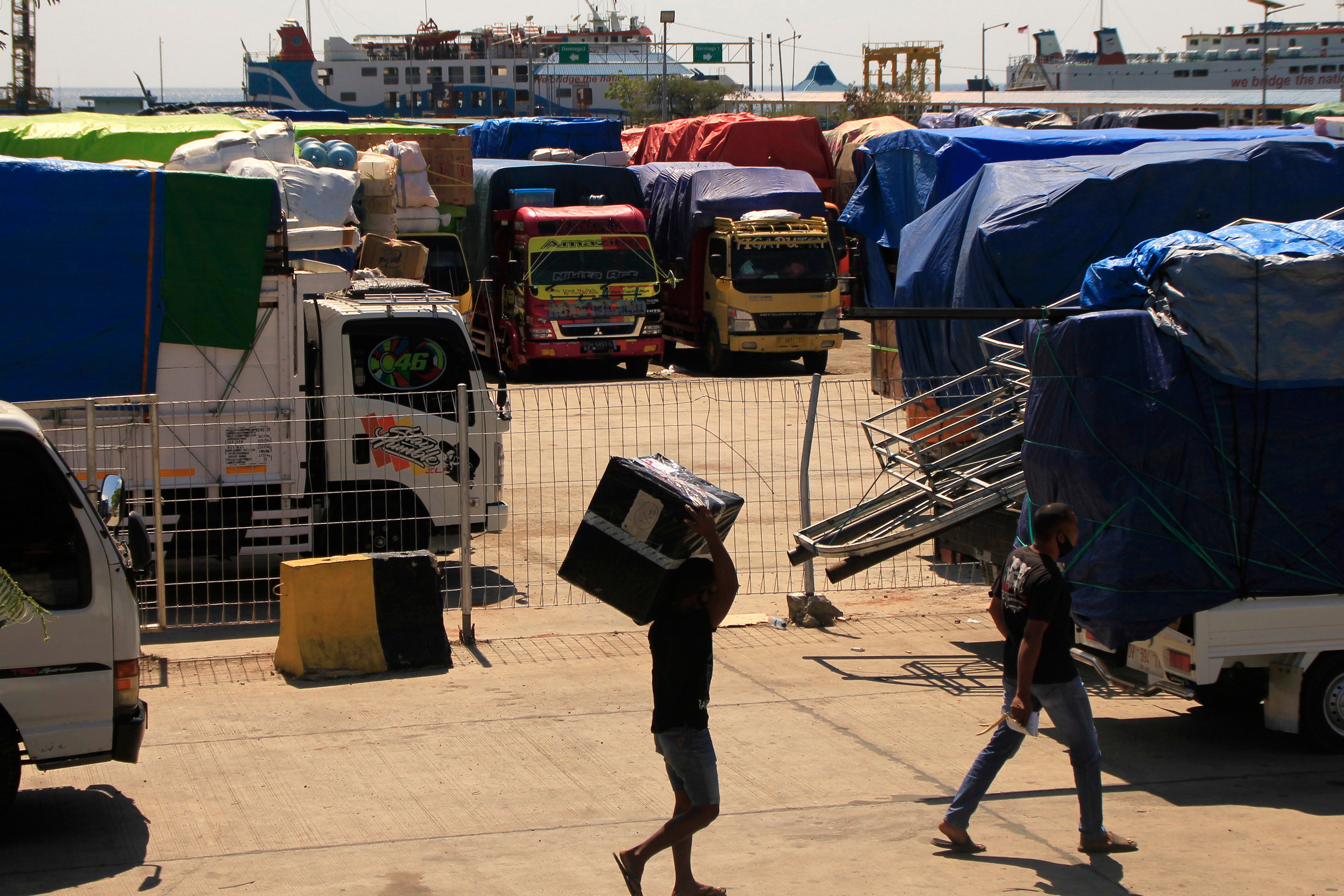 ejumlah pria berjalan di antara truk pembawa logistik antarpulau di NTT.