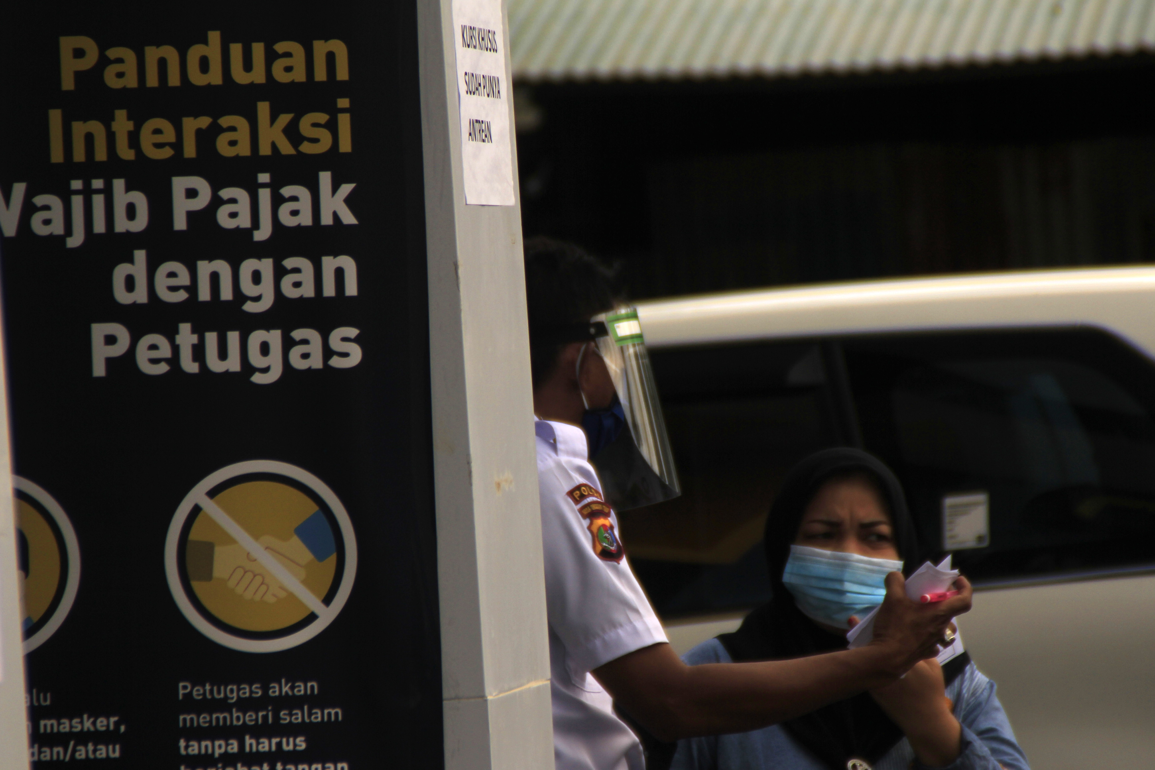 Seorang satpam menggunakan pelindung wajah menjelaskan tata cara pelayanan pajak di kantor Pelayanan Pajak (KPP) Pratama, Kupang, NTT.