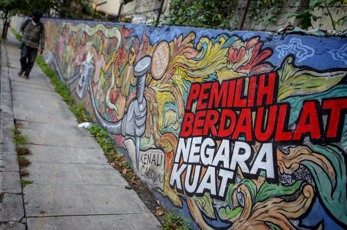 Warga melintas di depan mural bertema pemilihan umum di kawasan Pasar Anyar, Kota Tangerang, Banten, Kamis (7/5/2020).