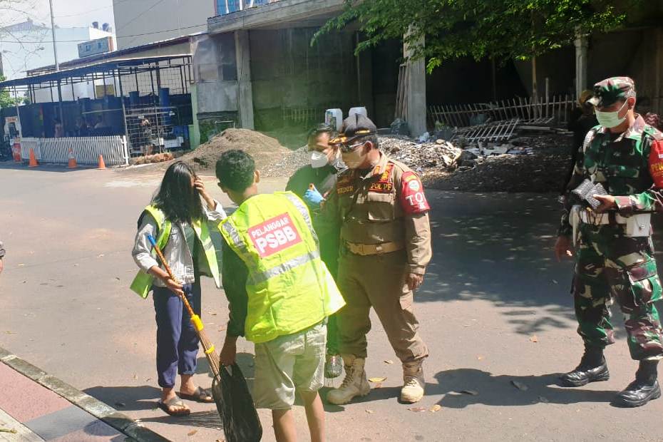 Gugus Tugas Percepatan Penanganan Covid-19 mengawasi warga yang diberi sanksi menyapu jalan karena tidak memakai masker.