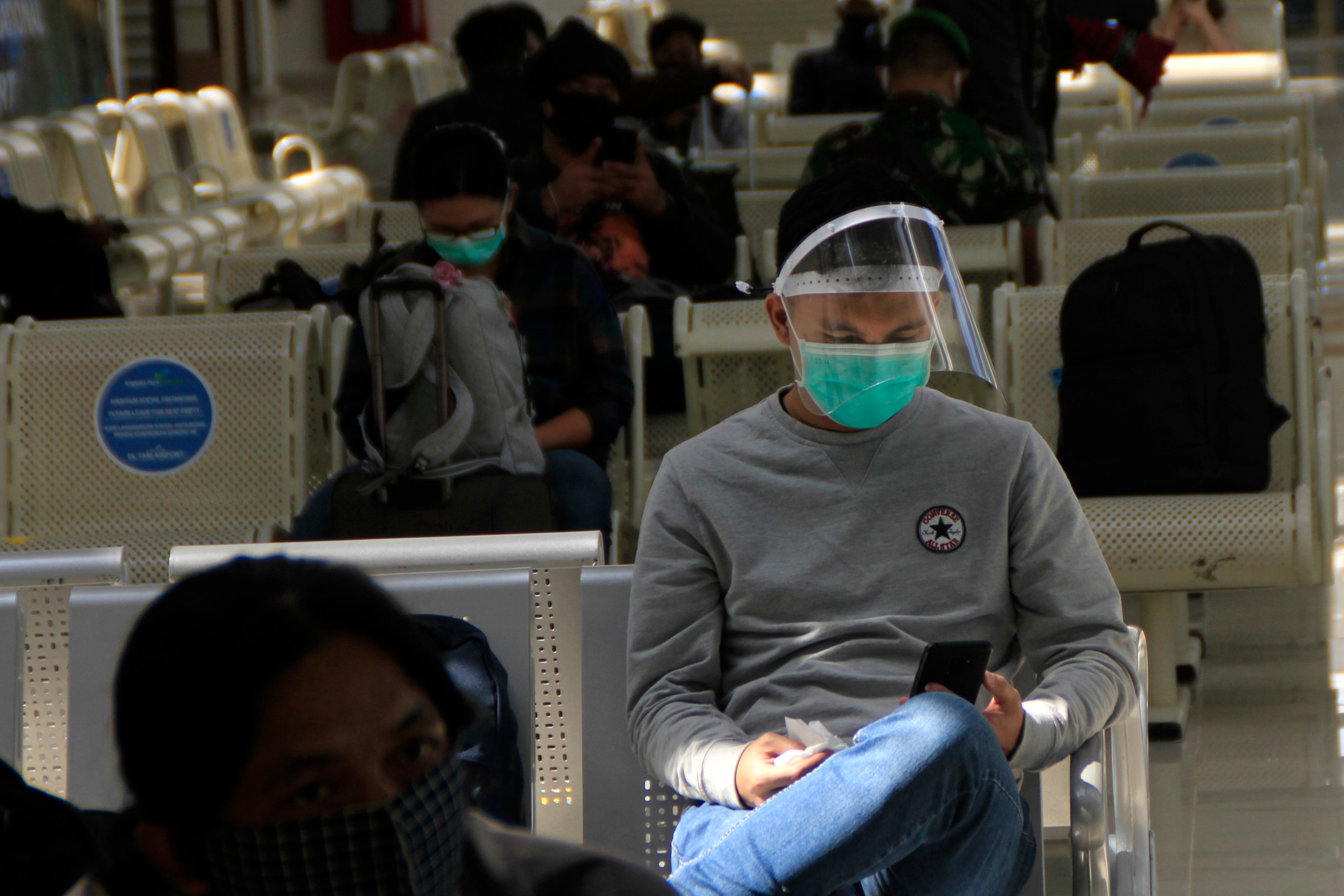 Seorang penumpang pesawat menggunakan pelindung wajah duduk di ruang tunggu keberangkatan bandara El Tari Kupang, NTT, Senin (8/6/2020).