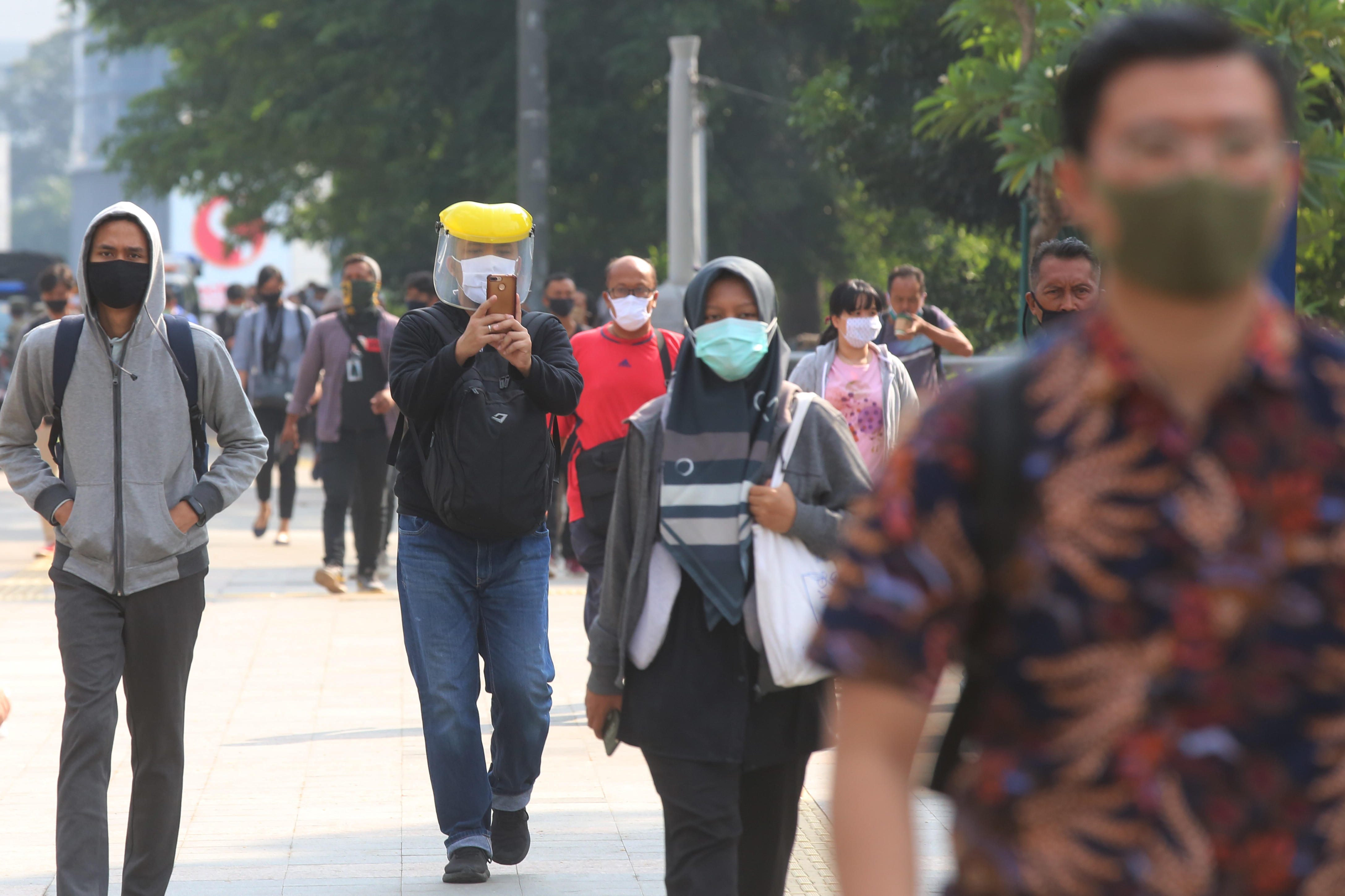 Pekerja menggunakan masker dan APD saat berjalan menuju kantornya, Senin (8/6) pagi