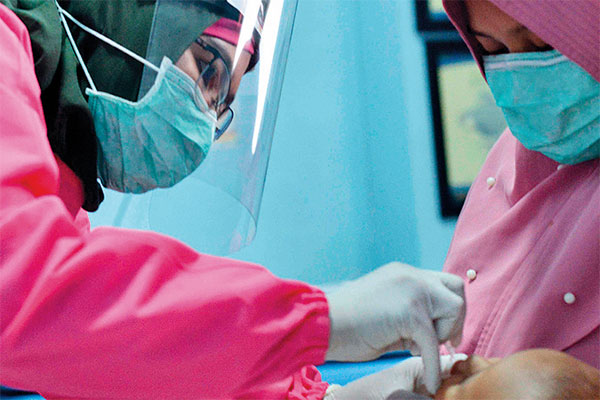 Petugas mengenakan alat pelindung diri saat memberikan vaksin polio pada bayi