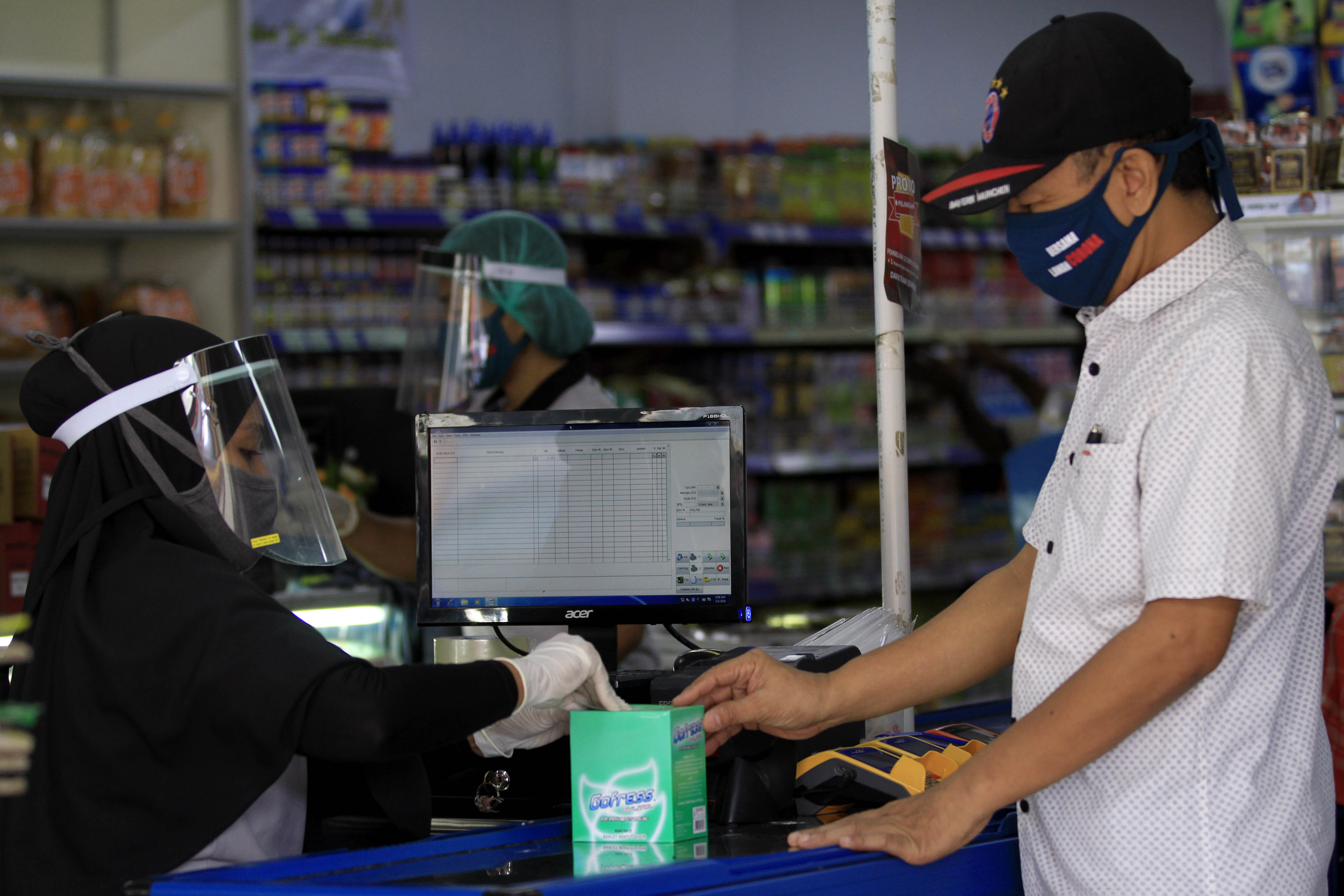 Seorang pramuniaga menggunakan pelindung wajah saat melayani pembeli di salah satu toko di Jayapura, Papua