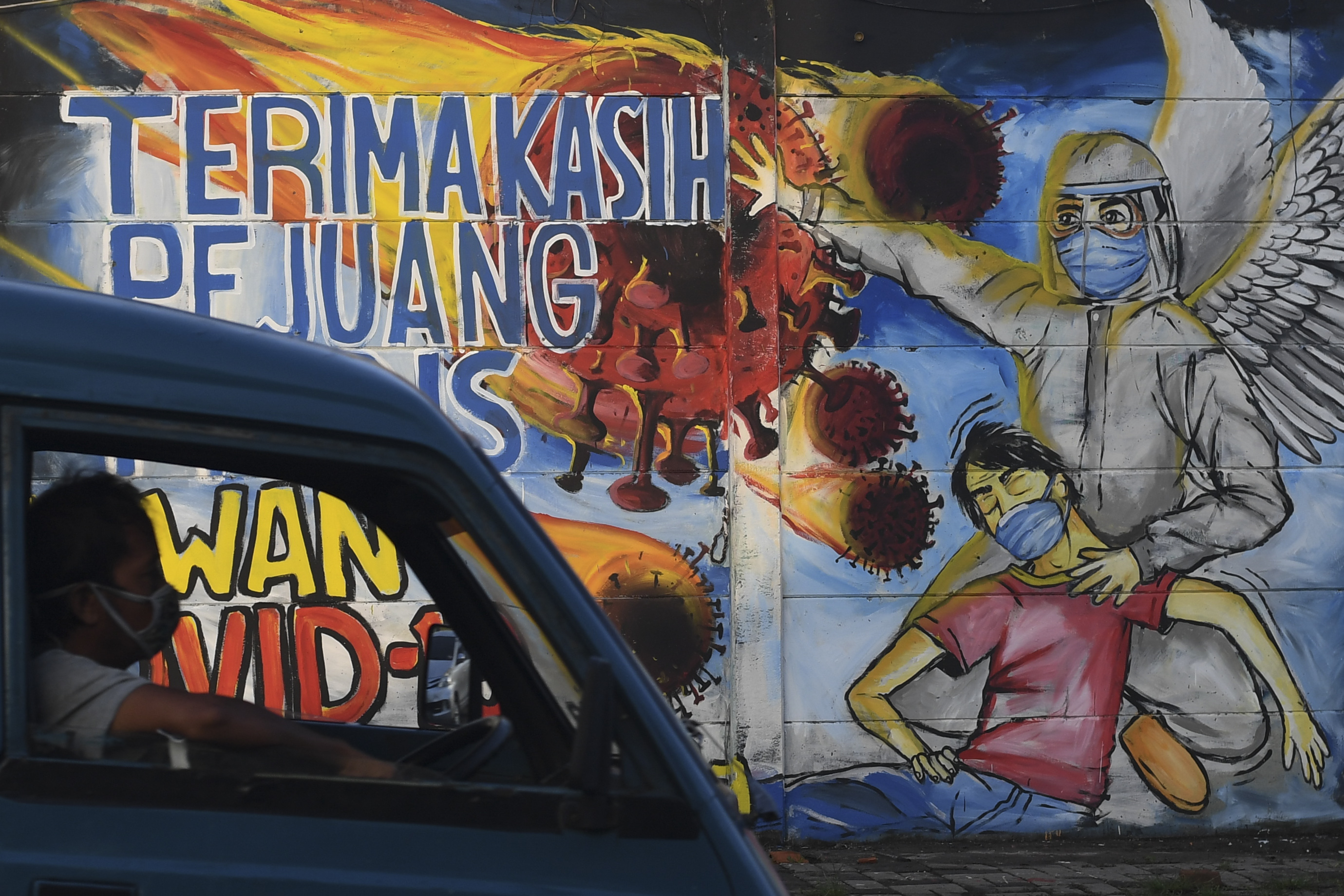 Pengemudi mobil melintasi mural kampanye covid-19 di Depok, Jawa Barat.