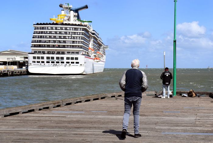 Seorang pria berdiri di pelabuhan Melbourne melihat kapal pesiar yang sedang berlabuh.  