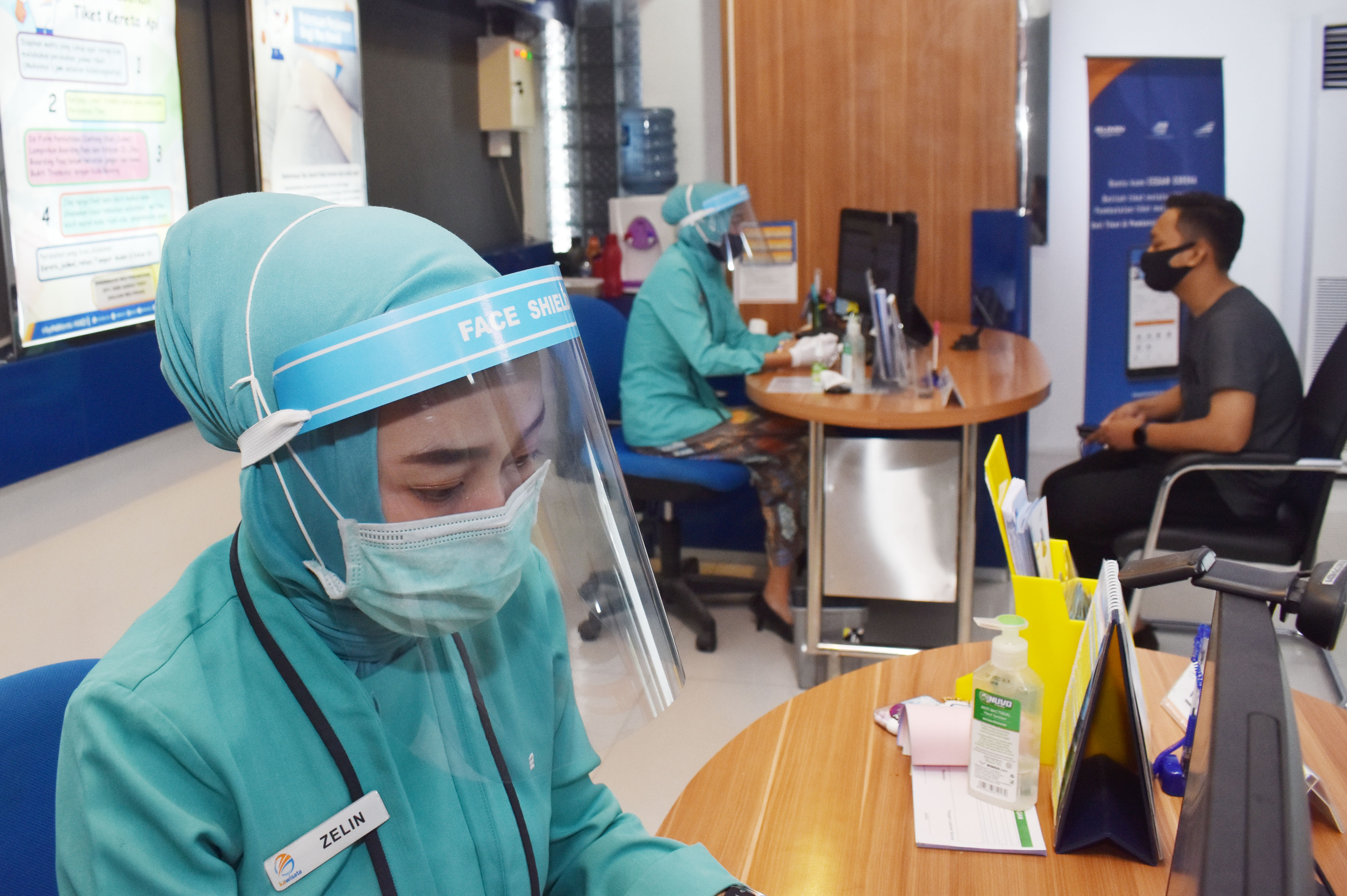 Petugas loket dengan menggunakan masker, pelindung wajah dan sarung tangan melayani konsumen di Stasiun Kereta Api (KA) Madiun, Jawa Timur.