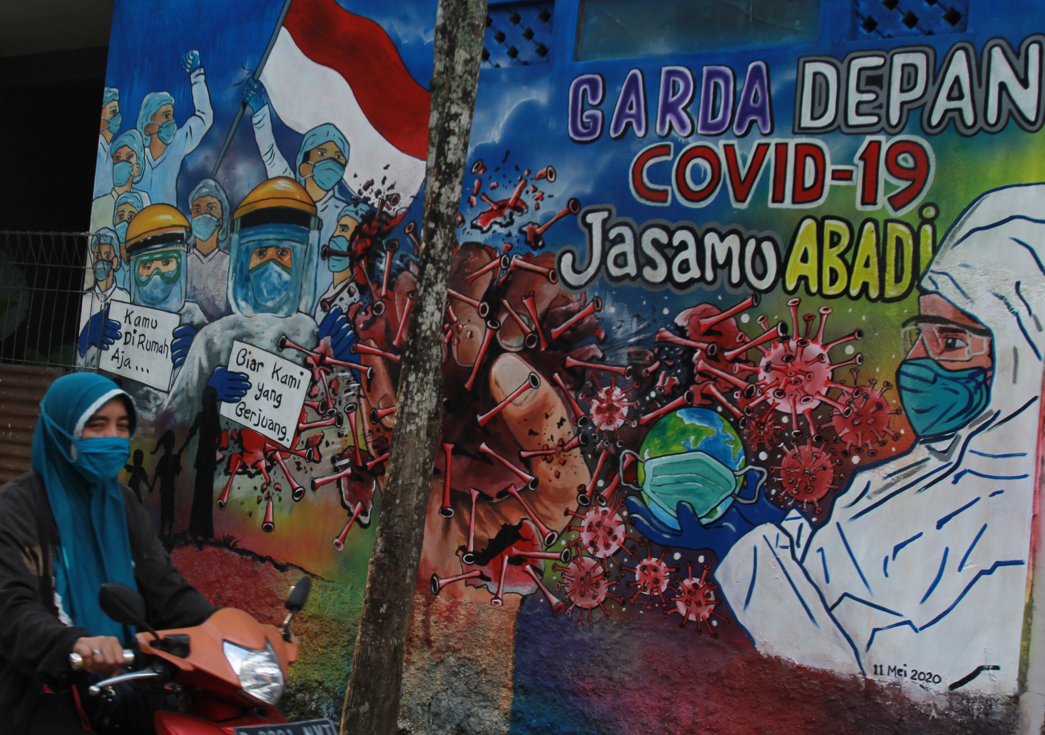 Pengendara di Pondok Aren, Tangerang, melintasi mural terkait dukungan terhadap tenaga medis.