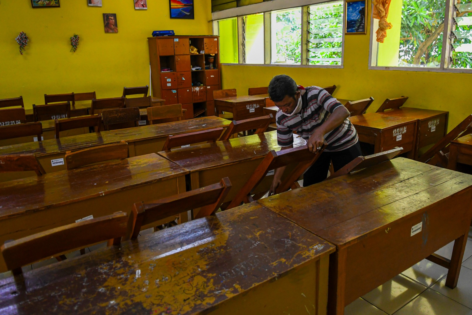 Petugas merapikan kursi diruang kelas SMP 216 Jakarta Pusat, Senin (16/3/2020). 