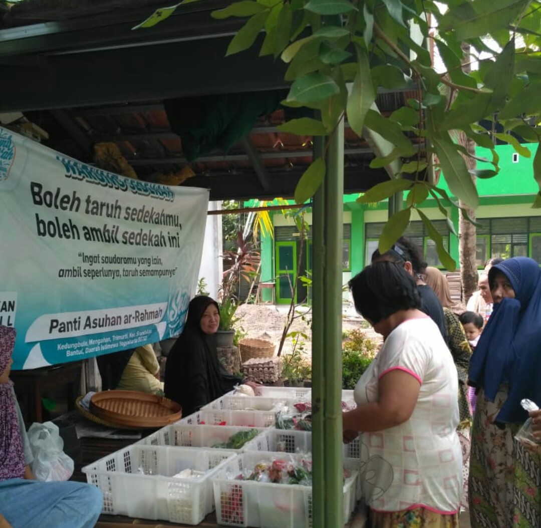 Euis Nurtrisnawati menyambut warga sekitar yang sedang memilih paket lauk pauk yang digelar lewat warung sedekah di depan rumahnya. 