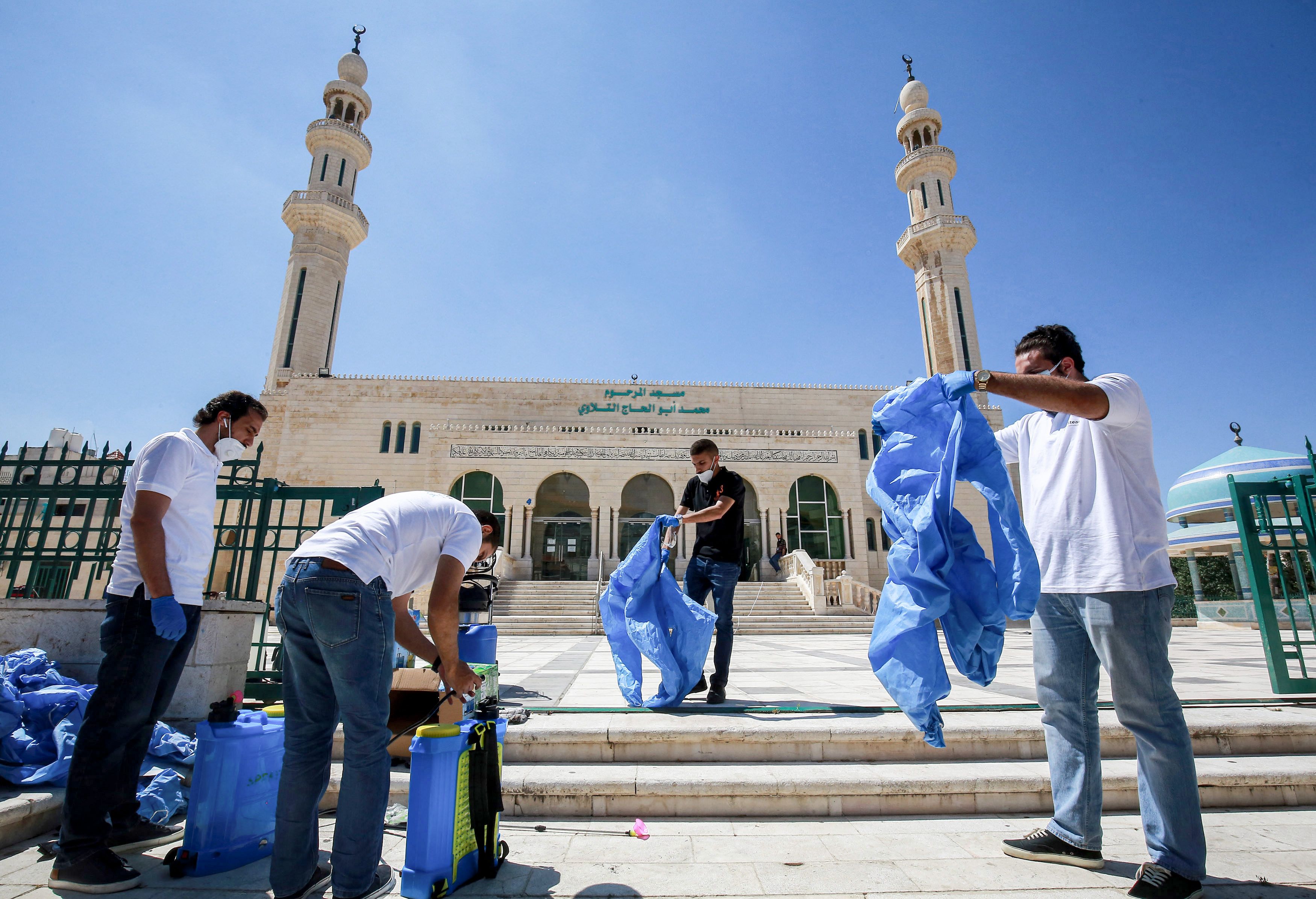 Petugas memakai APD sebelum menyemprotkan disinfektan ke masjid di Amman yang mulai dibuka lagi