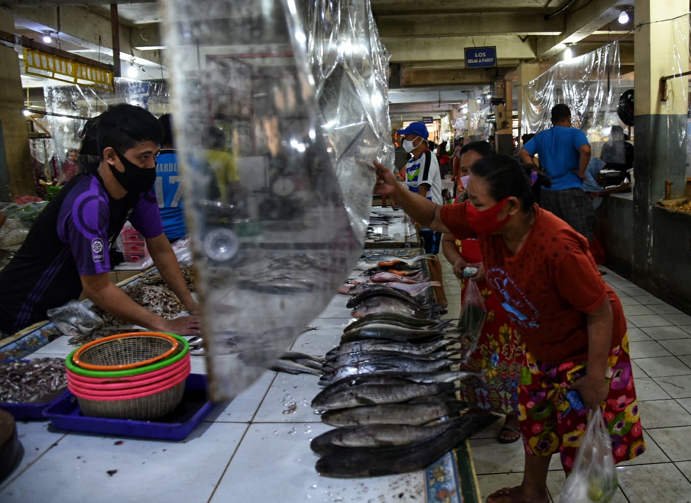 Penjual ikan melayani konsumen dari balik tirai plastik di area kios Pasar Bandeng, Kota Tangerang, Banten.