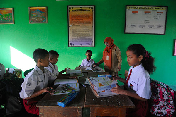 Seorang guru sedang memberikan arahan kepada muridnya di sekolah, sebelum masa pandemi covid-19
